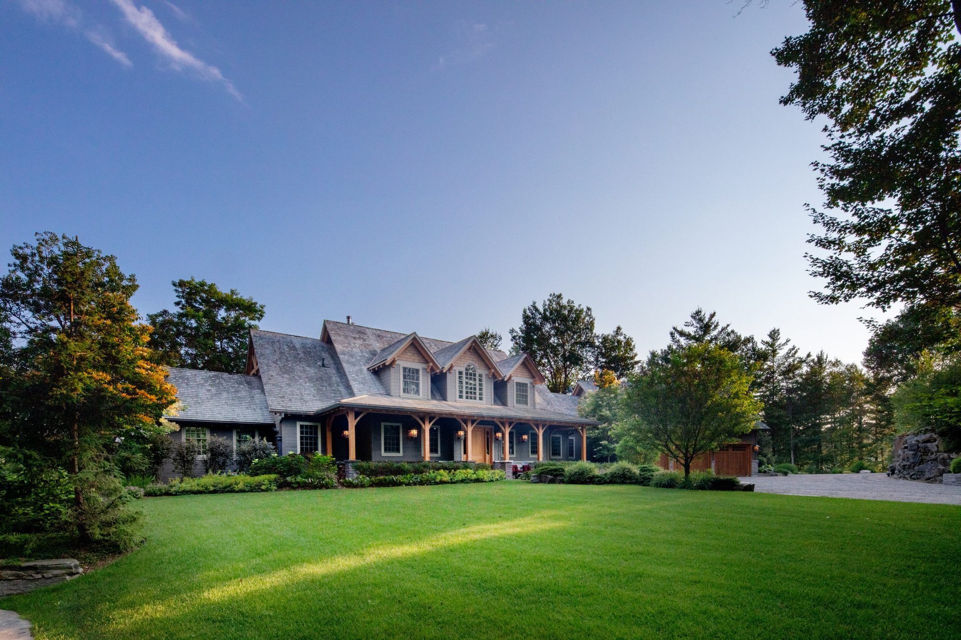 Large gray house with a wraparound porch and manicured green lawn at dusk