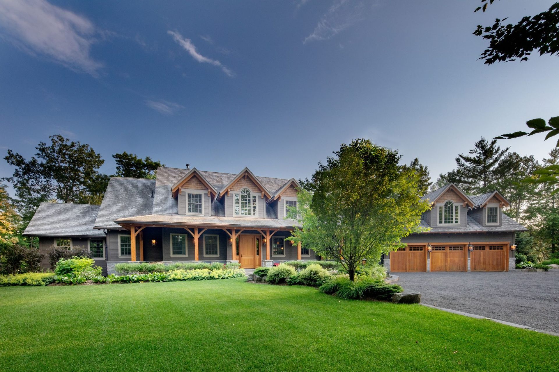 Large gray house with a front porch and green lawn under a clear blue sky