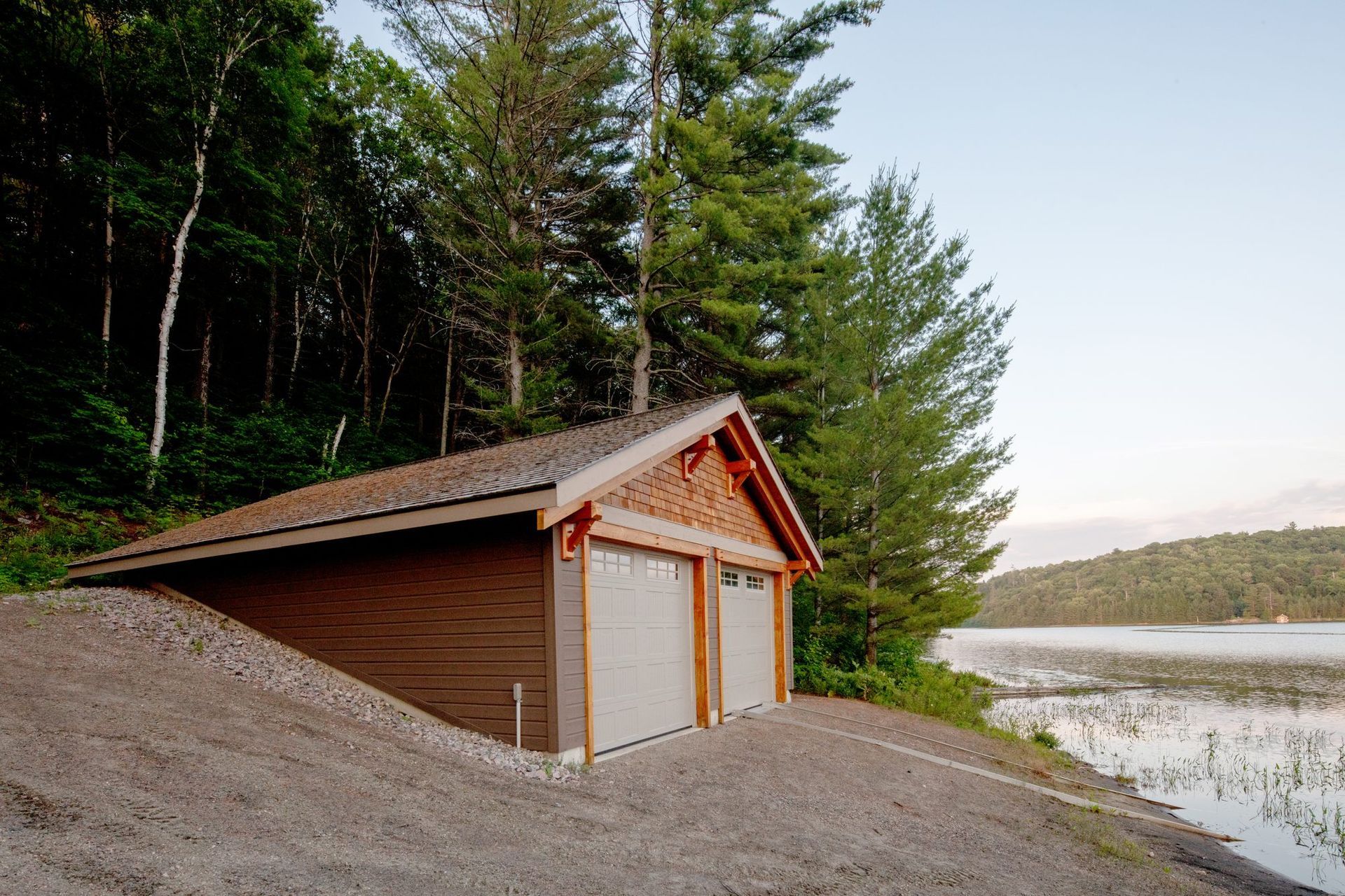 Wooden garage by a lakeshore, nestled beside a forest on a gravel slope