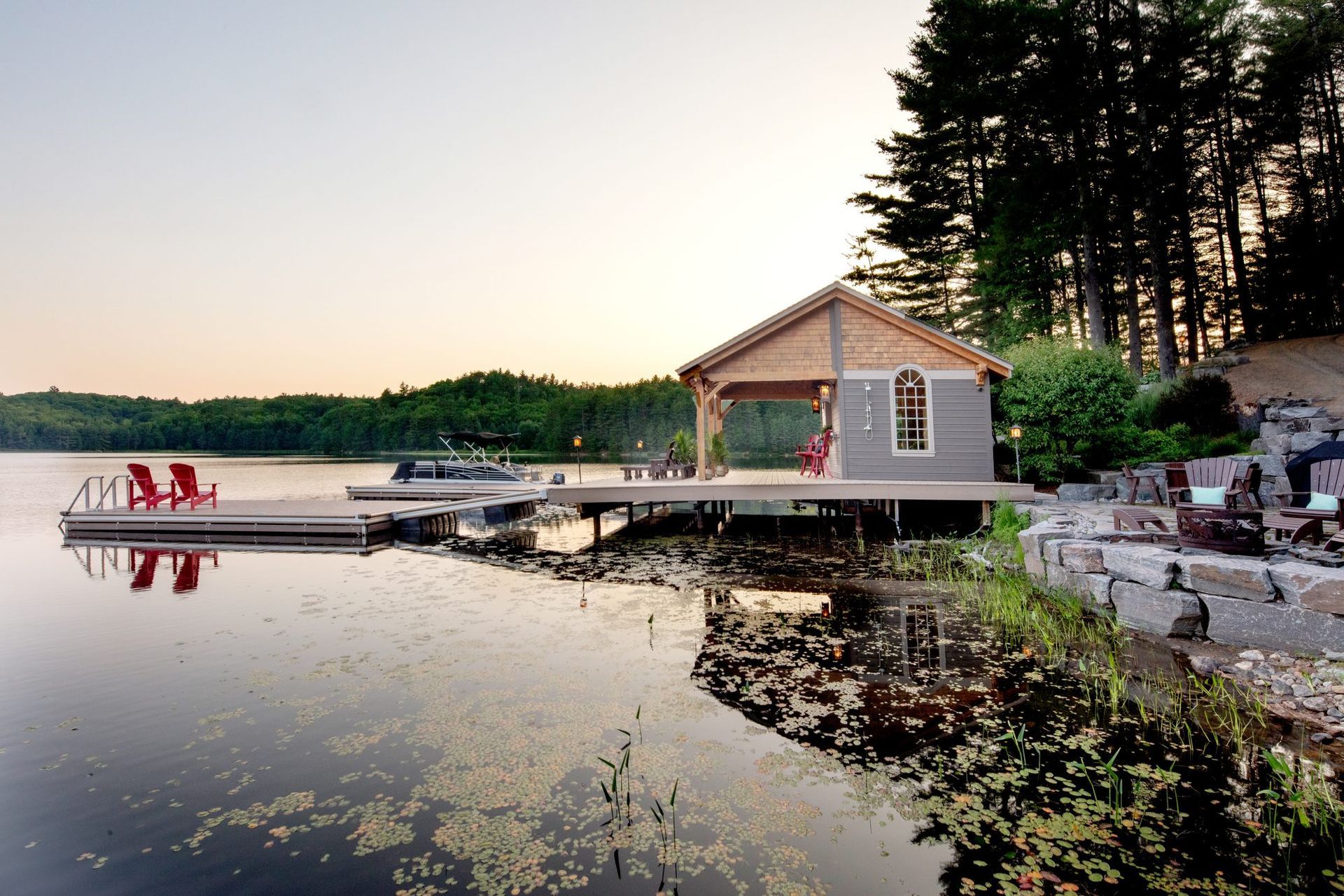 Lakeside dock at sunset beside a small cabin, with calm water and trees reflecting in the shore.