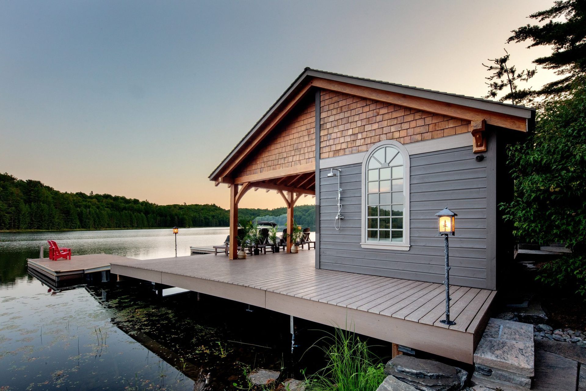 Lakeside cabin deck at sunset with a dock and calm water, lit by a small lamp