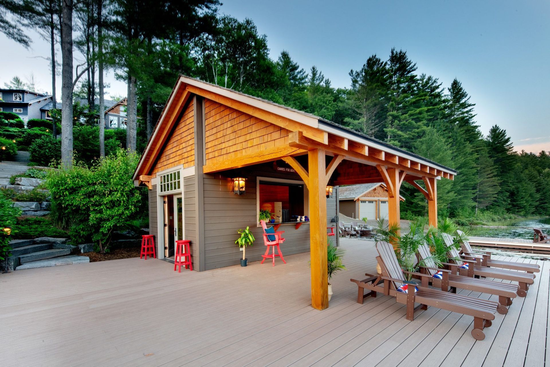 Outdoor patio with wooden pavilion, lounge chairs, and tables beside a small building at sunset