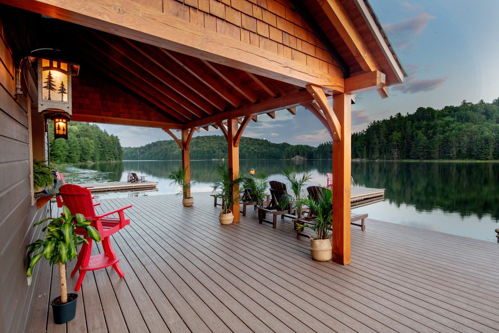 Covered lakeside deck with red chairs, potted plants, and a calm view of the water at dusk