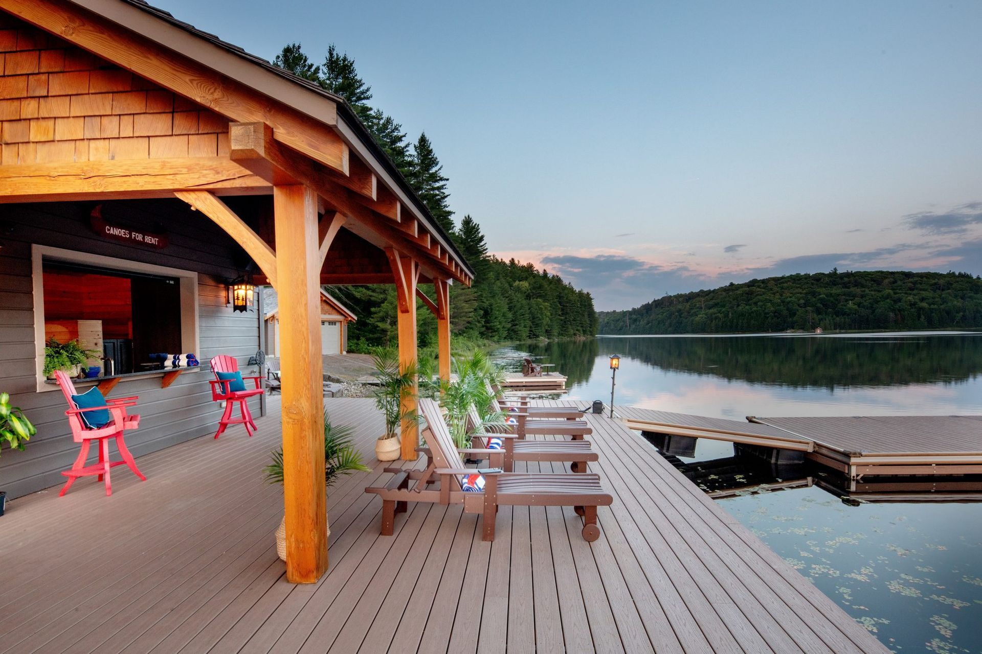 Lakeside deck with picnic tables beside a wooden pavilion at sunset, overlooking calm water and forested hills