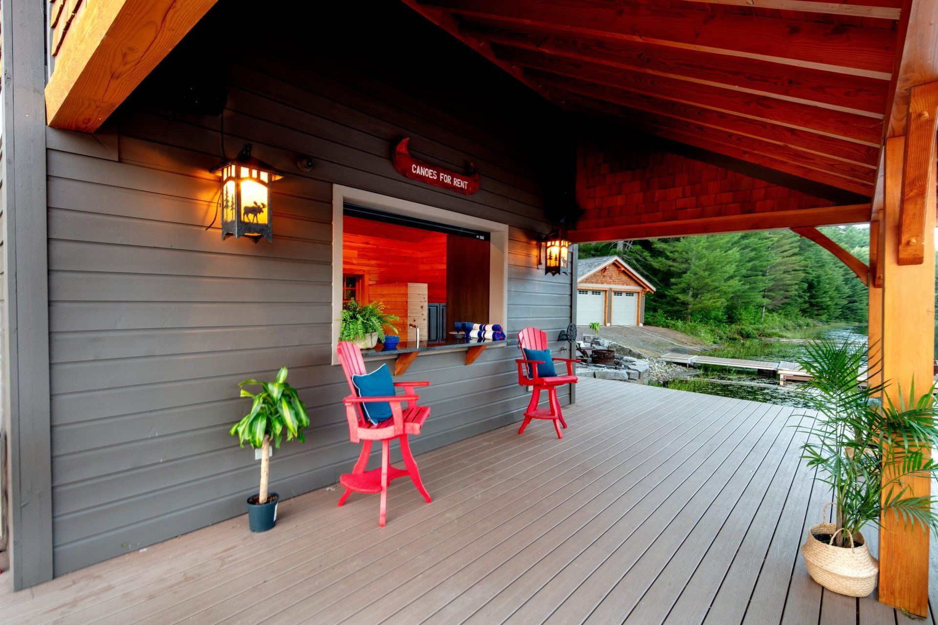 Covered cabin porch with red chairs, potted plants, and a wooden deck overlooking greenery