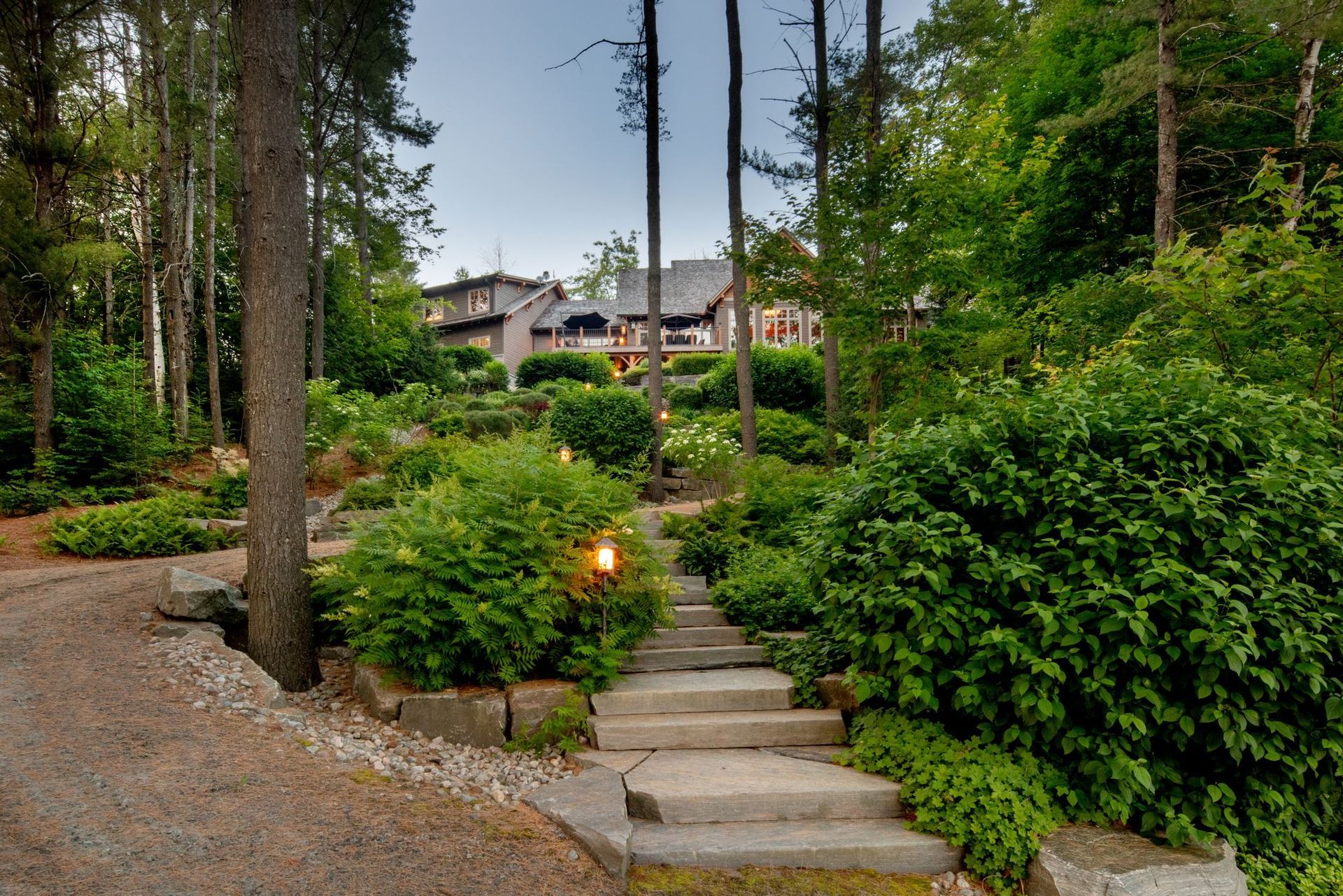 Stone steps lead through a wooded garden toward a house at dusk.