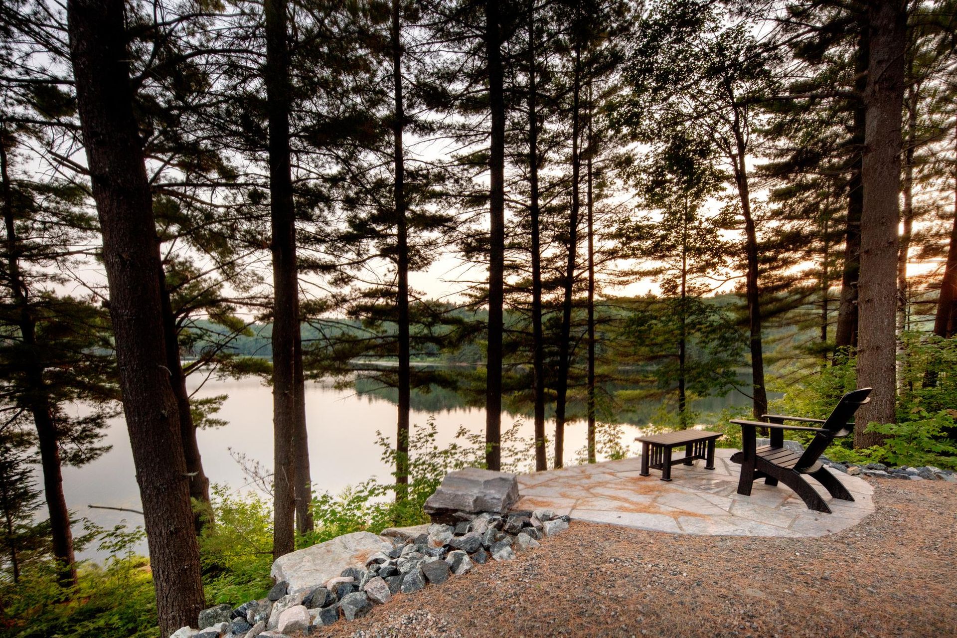 Wooded lakeside patio with Adirondack chairs at sunset