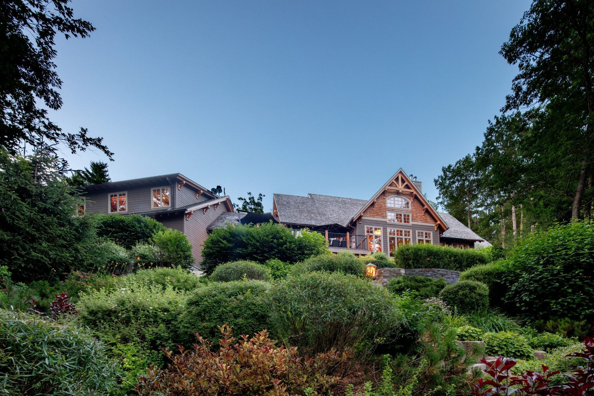 Stone house with a steep roof behind lush green gardens under a clear blue sky