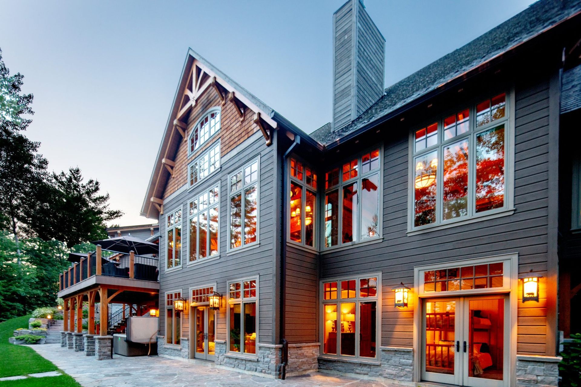Modern stone and wood house with large lit windows at dusk