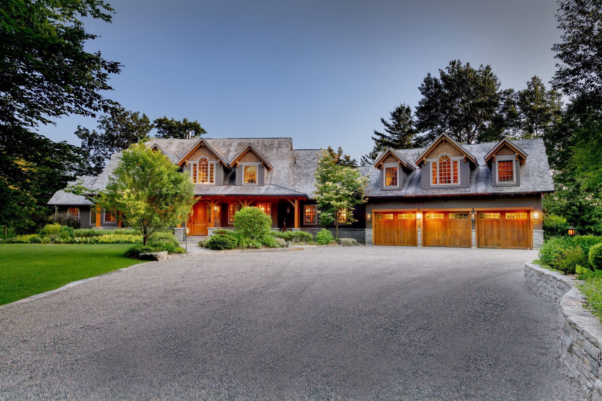 Large country house with gray roof, red front door, and attached three-car garage beside a gravel driveway