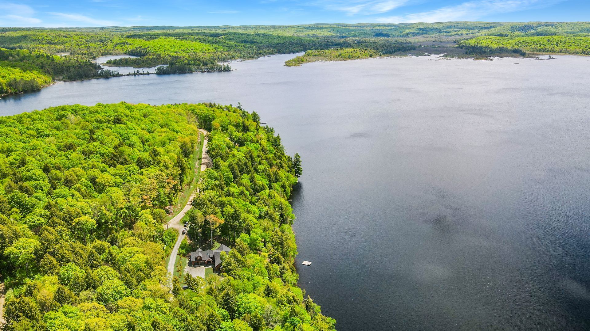 Aerial view of a winding road beside a forested lake with green hills in the distance