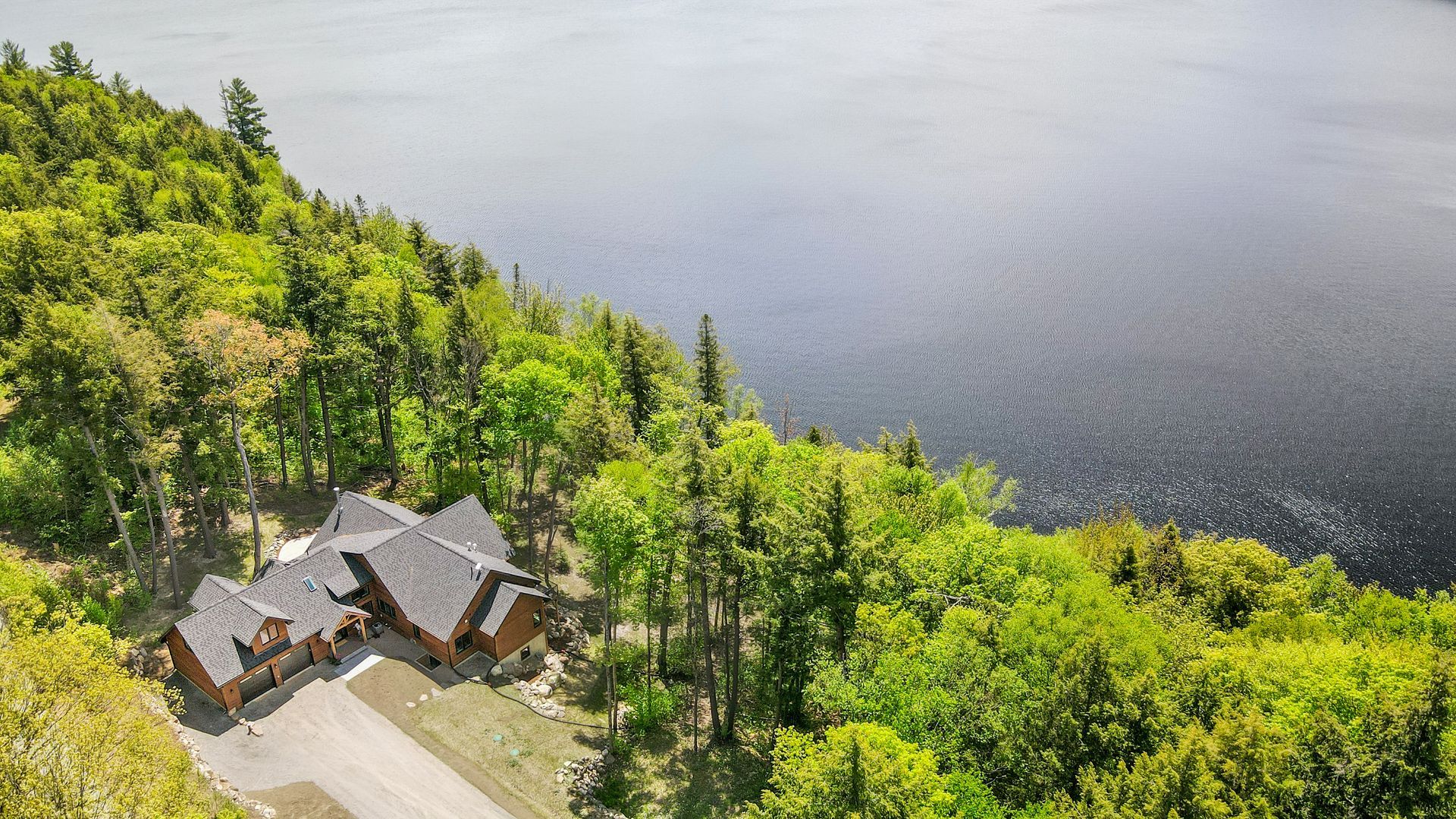 Aerial view of a lakeside house surrounded by green trees beside dark water.
