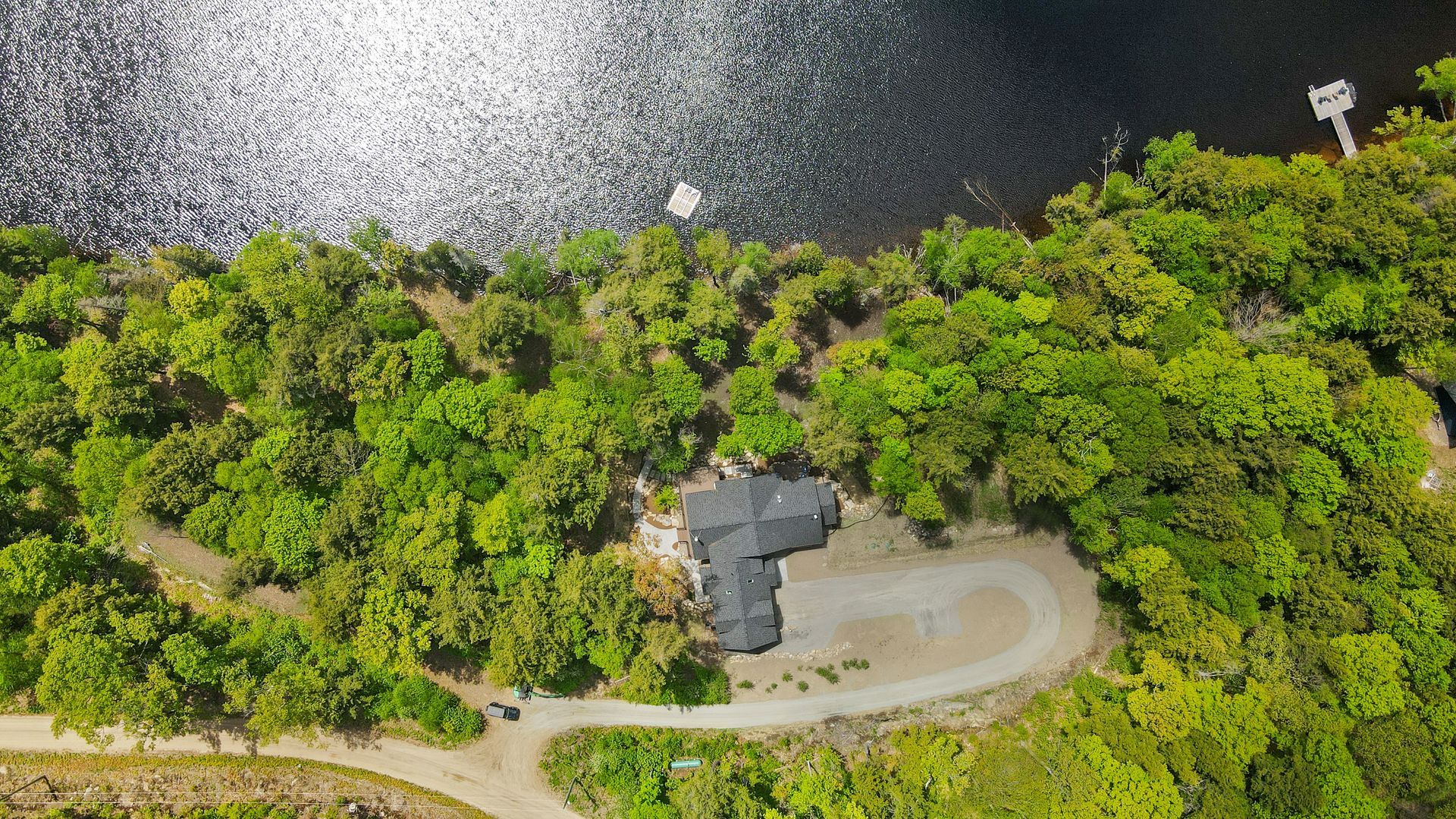 Aerial view of a forested lakeside road with a small building and winding dirt path.