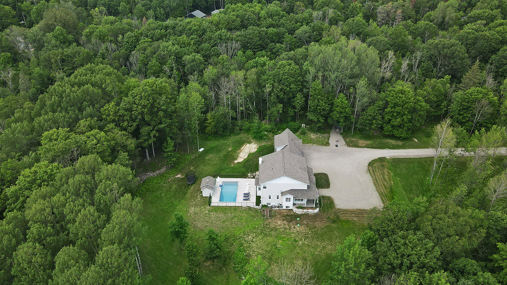 Aerial view of a lakeside house surrounded by green trees beside dark water.