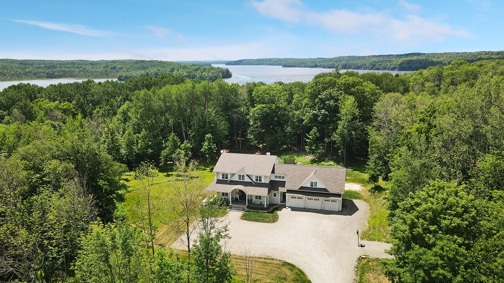 Aerial view of a forested lakeside road with a small building and winding dirt path.