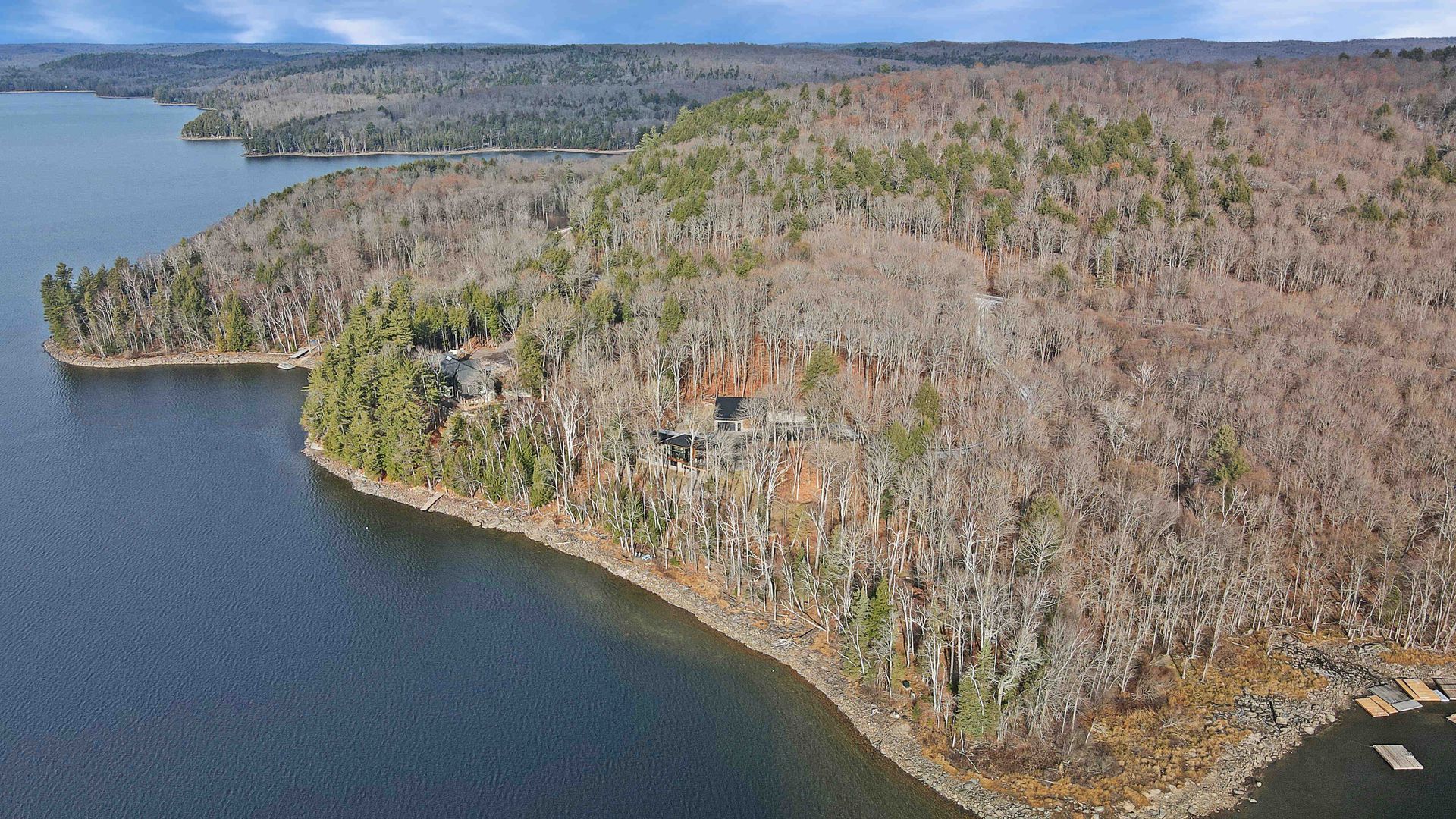 Aerial view of a forested rocky shoreline beside a calm blue lake