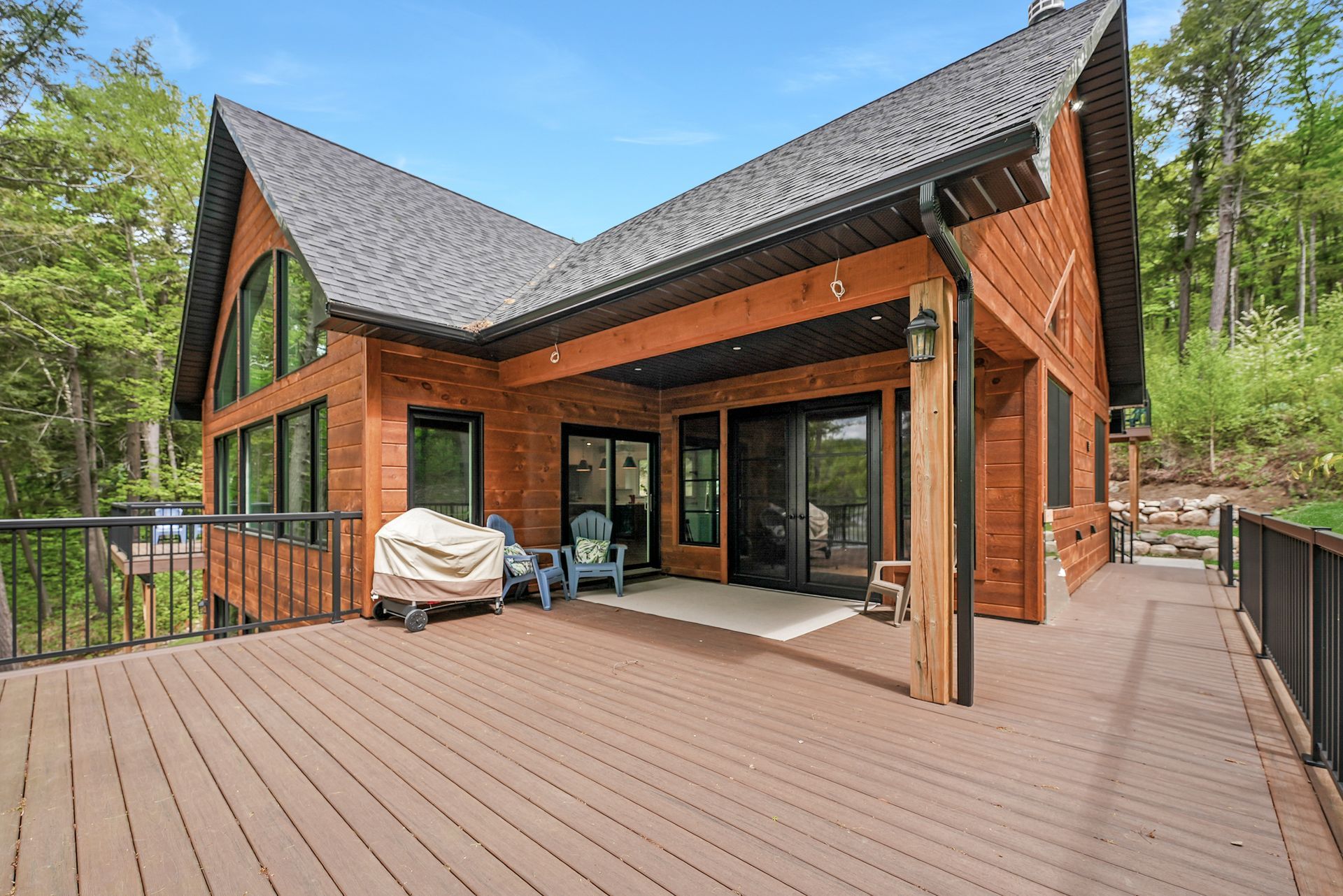 Modern wood cabin with large deck, sliding glass doors, and forest surroundings