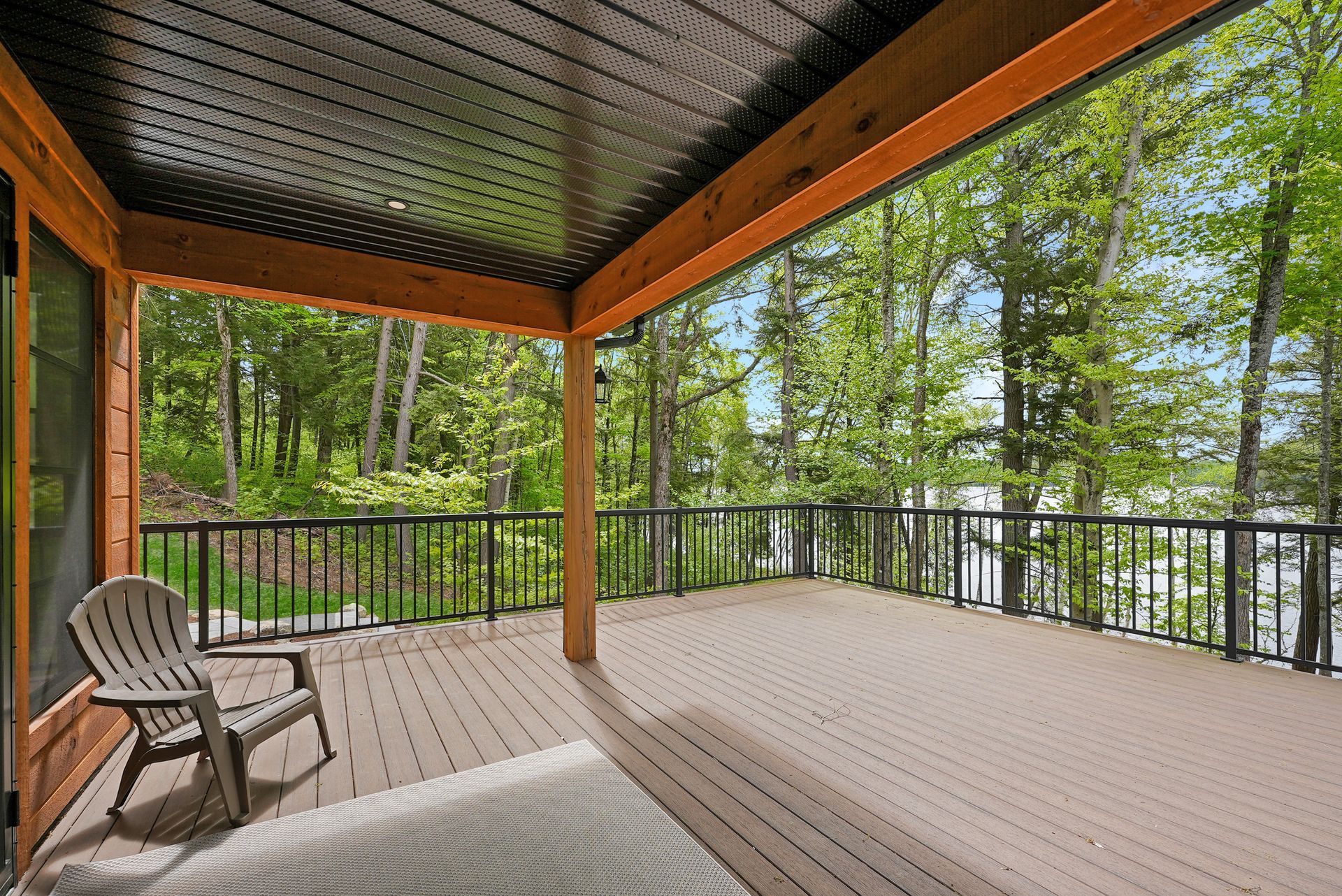 Covered wooden deck overlooking a wooded backyard, with a chair and black railing.