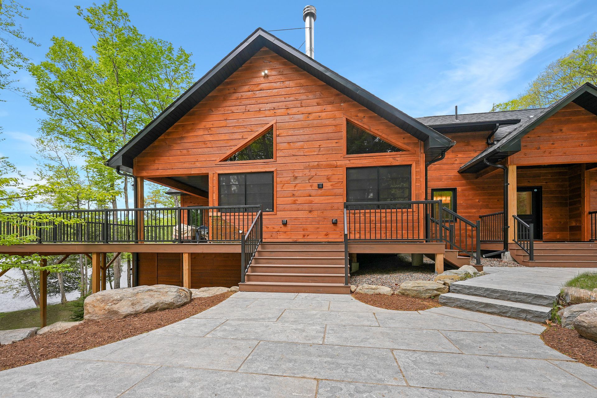 Modern wooden cabin with deck, stone steps, and a gravel path under a blue sky
