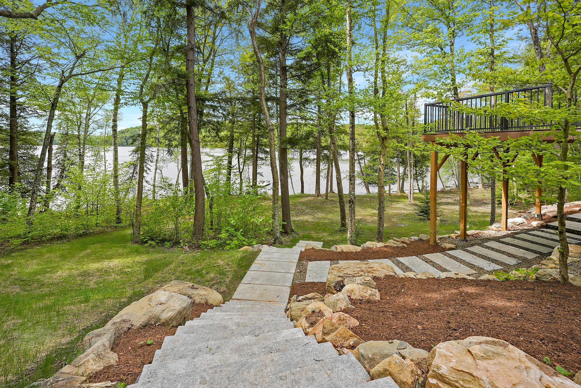 Stone walkway in a wooded park beside steps, rocks, and a wooden deck overlooking trees.