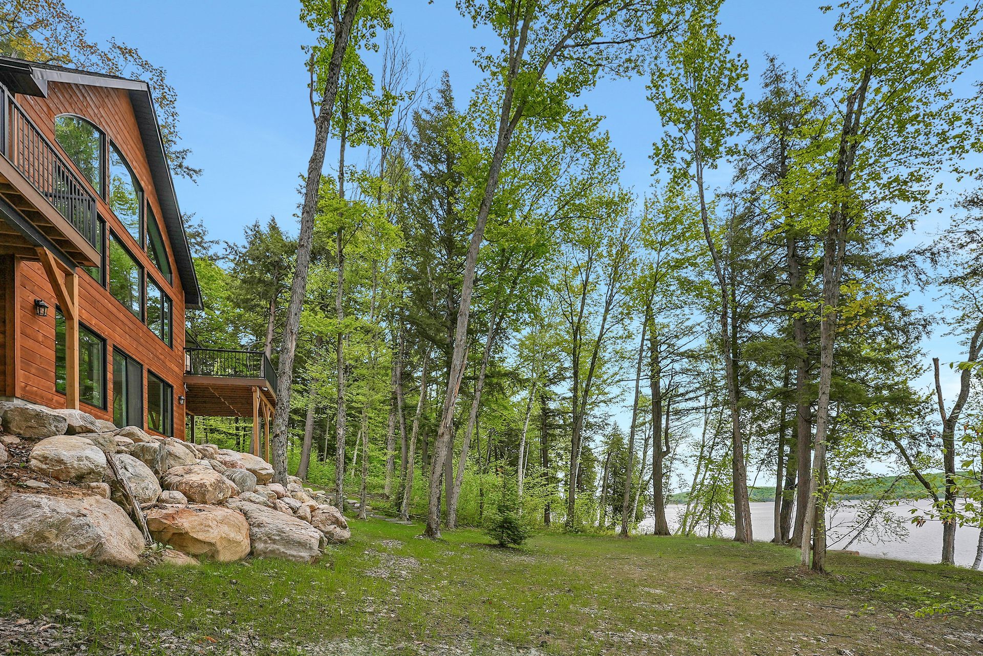 Wooden cabin beside rocky shoreline and birch trees under a clear blue sky