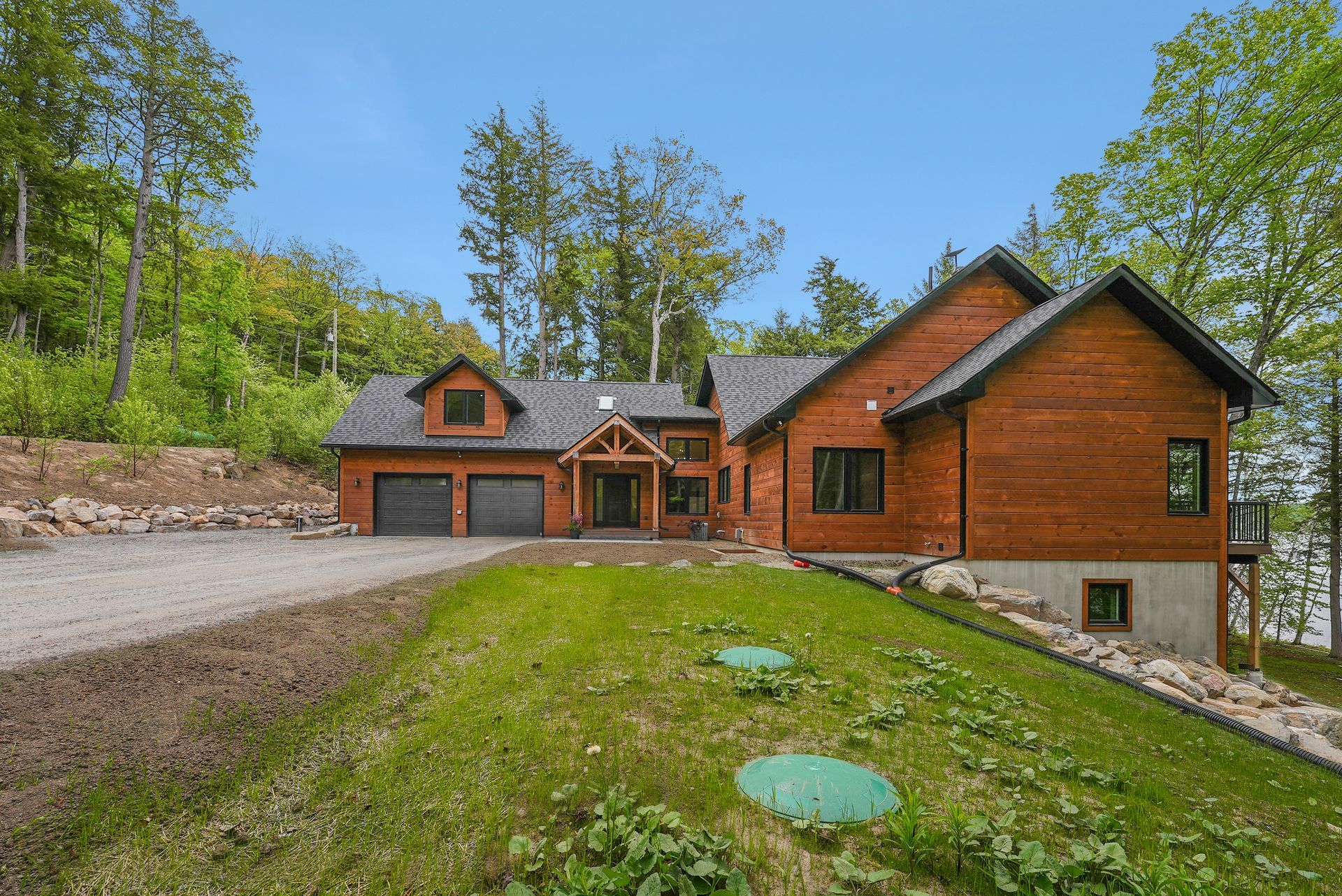 Rustic log cabin home with garage, stone driveway, and green lawn under a clear blue sky