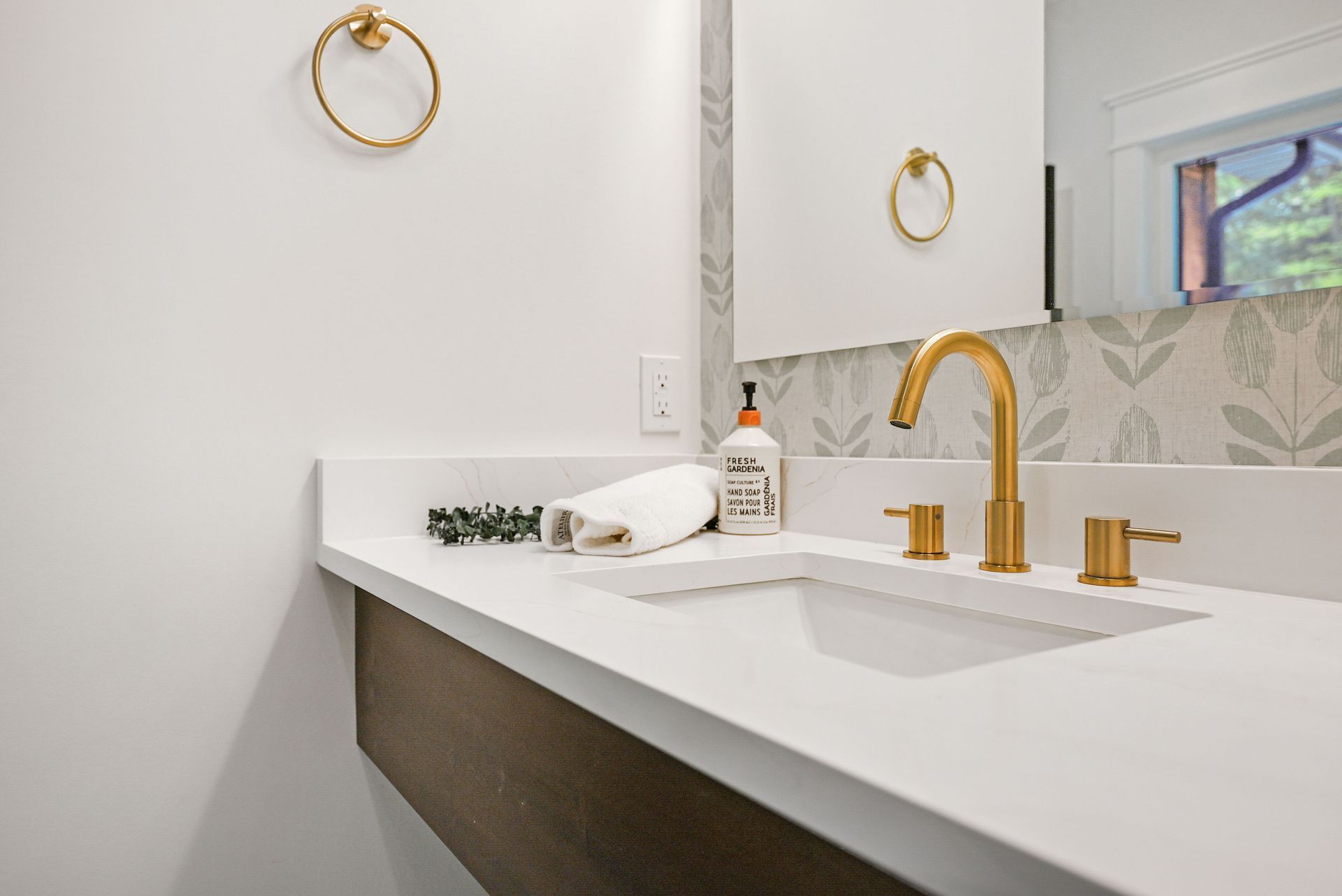 Modern bathroom vanity with white sink, gold faucet, round mirror, and soap dispenser