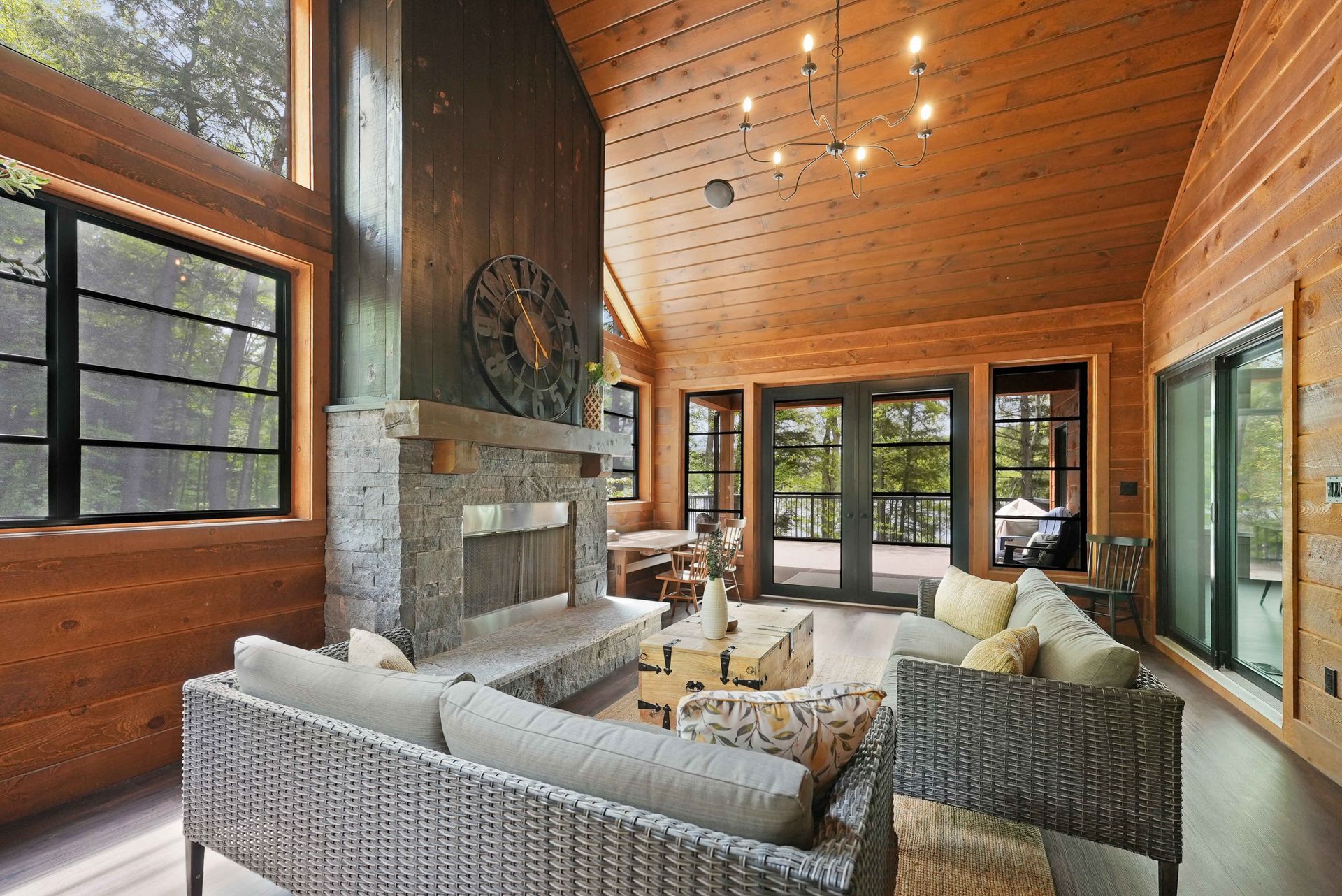 Cozy wood-paneled living room with stone fireplace, large windows, and wicker seating