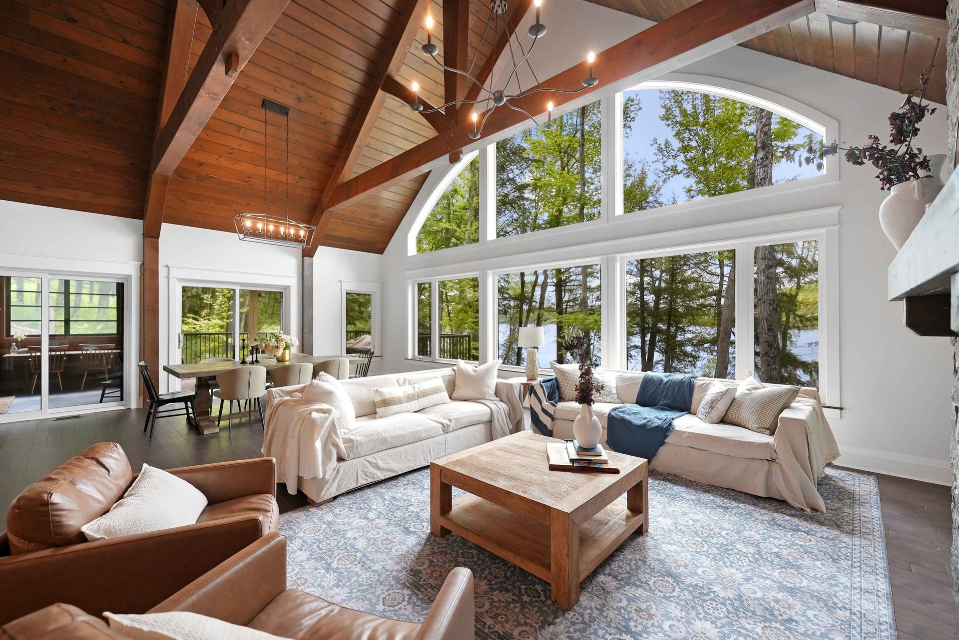 Bright living room with vaulted wood ceiling, white sofas, large windows, and a coffee table
