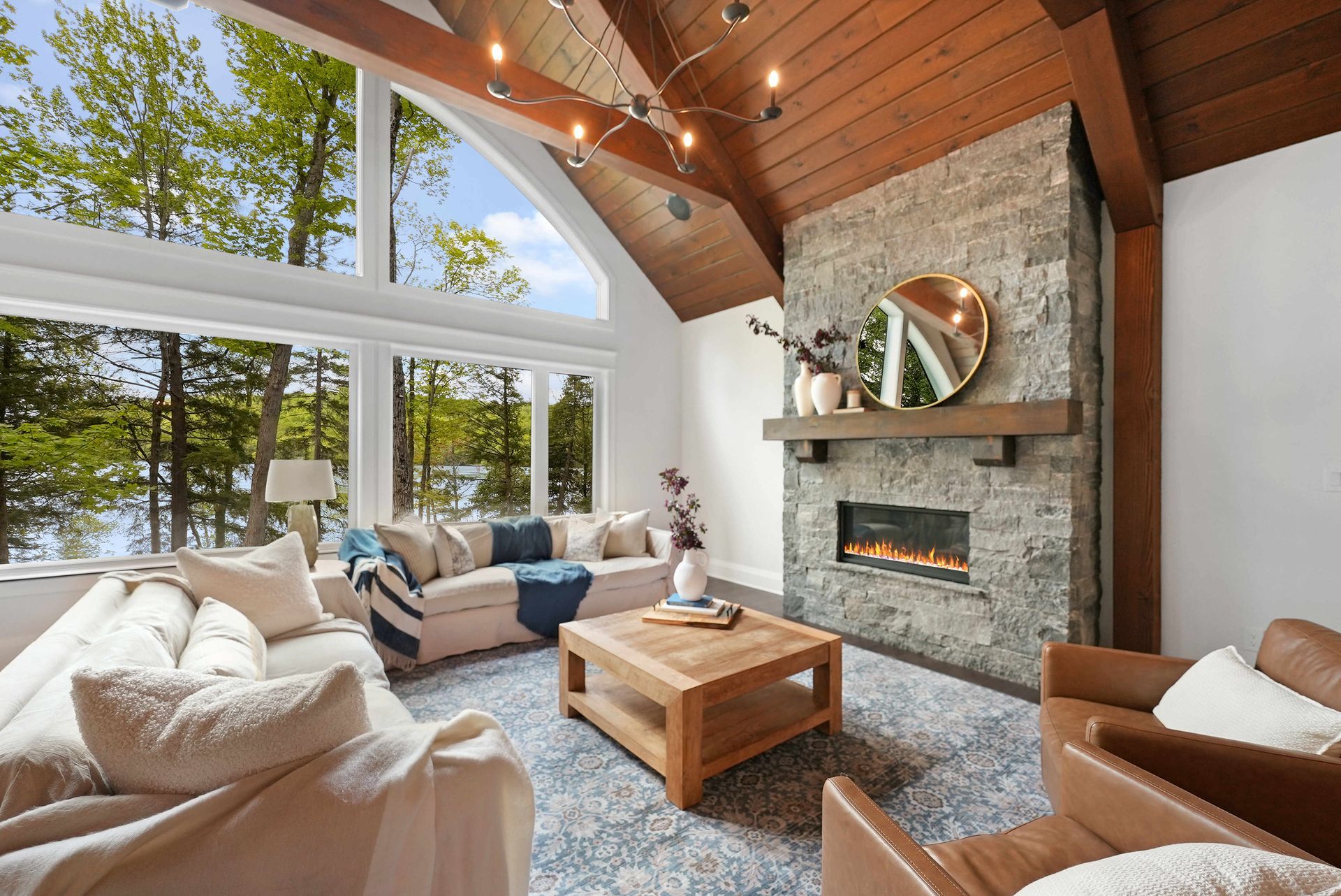 Bright living room with vaulted wood ceiling, stone fireplace, large windows, and cozy seating
