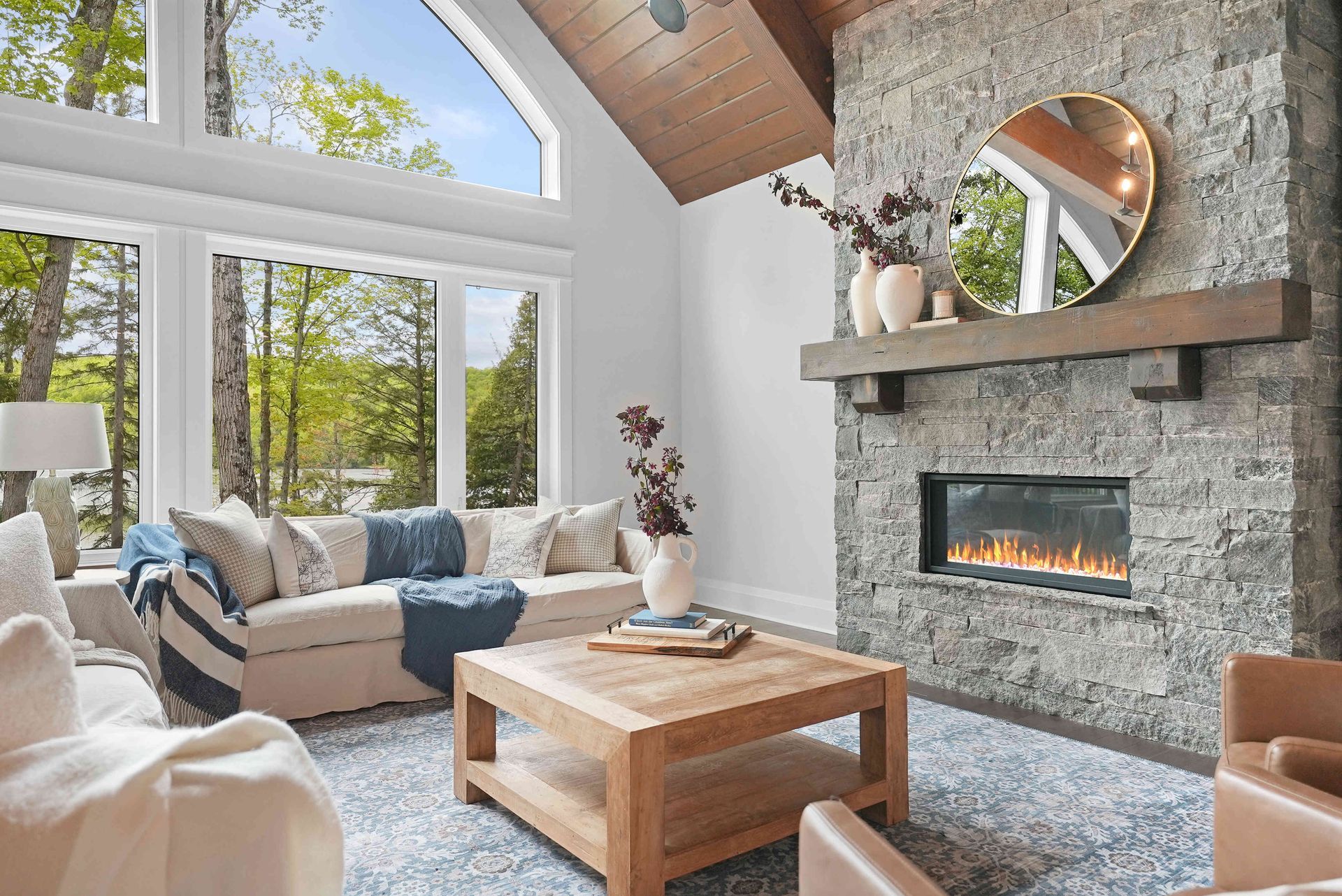 Bright living room with stone fireplace, large windows, wood coffee table, and beige sectional seating