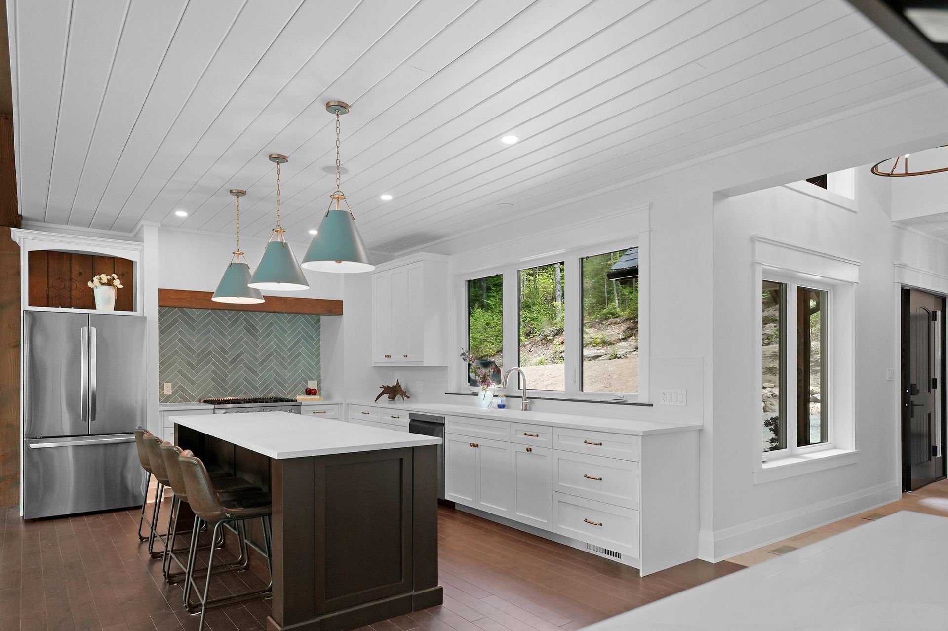 Bright modern kitchen with white cabinets, dark island, stainless fridge, and pendant lights