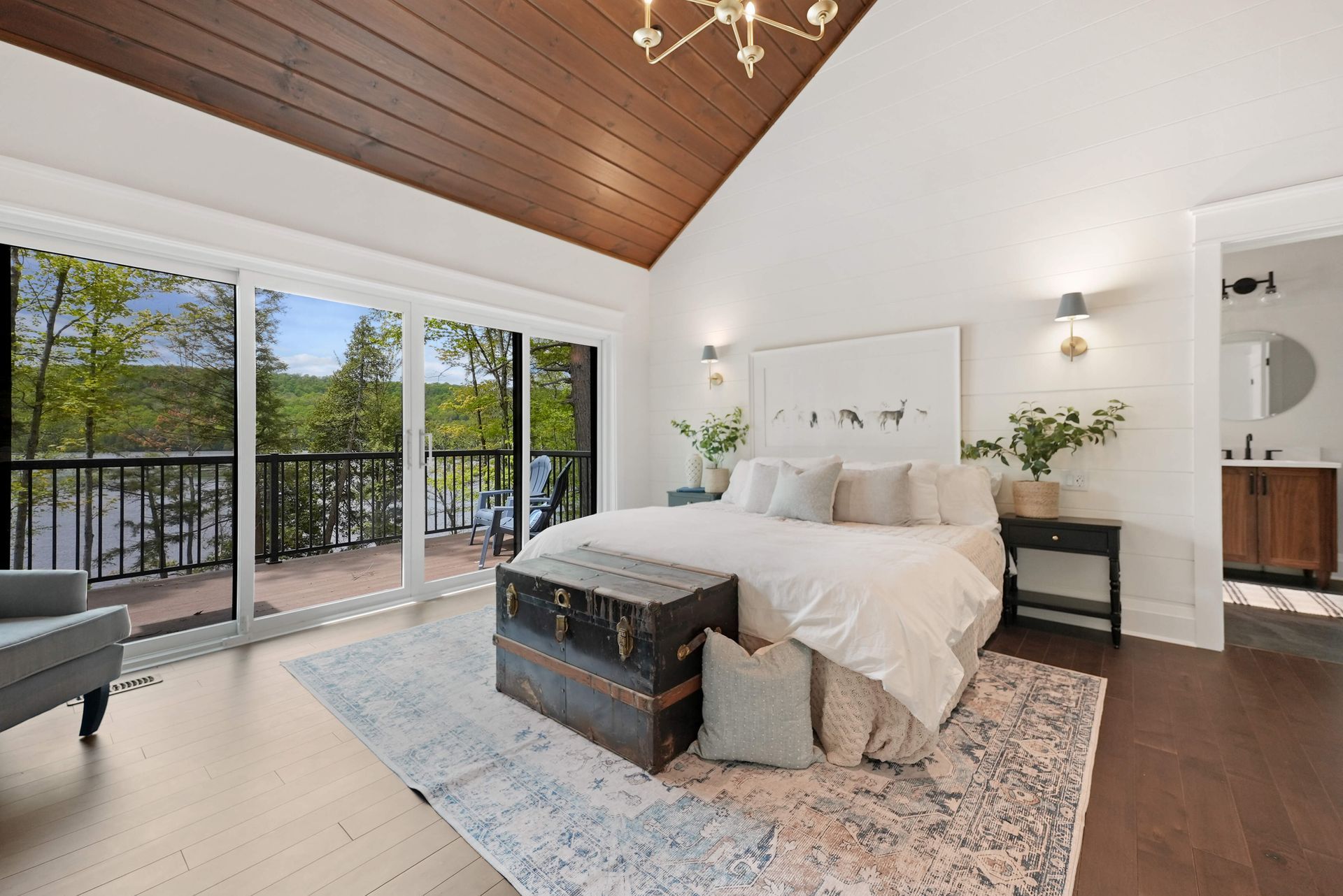 Bright bedroom with vaulted wood ceiling, white bed, gray rug, and sliding doors to a balcony