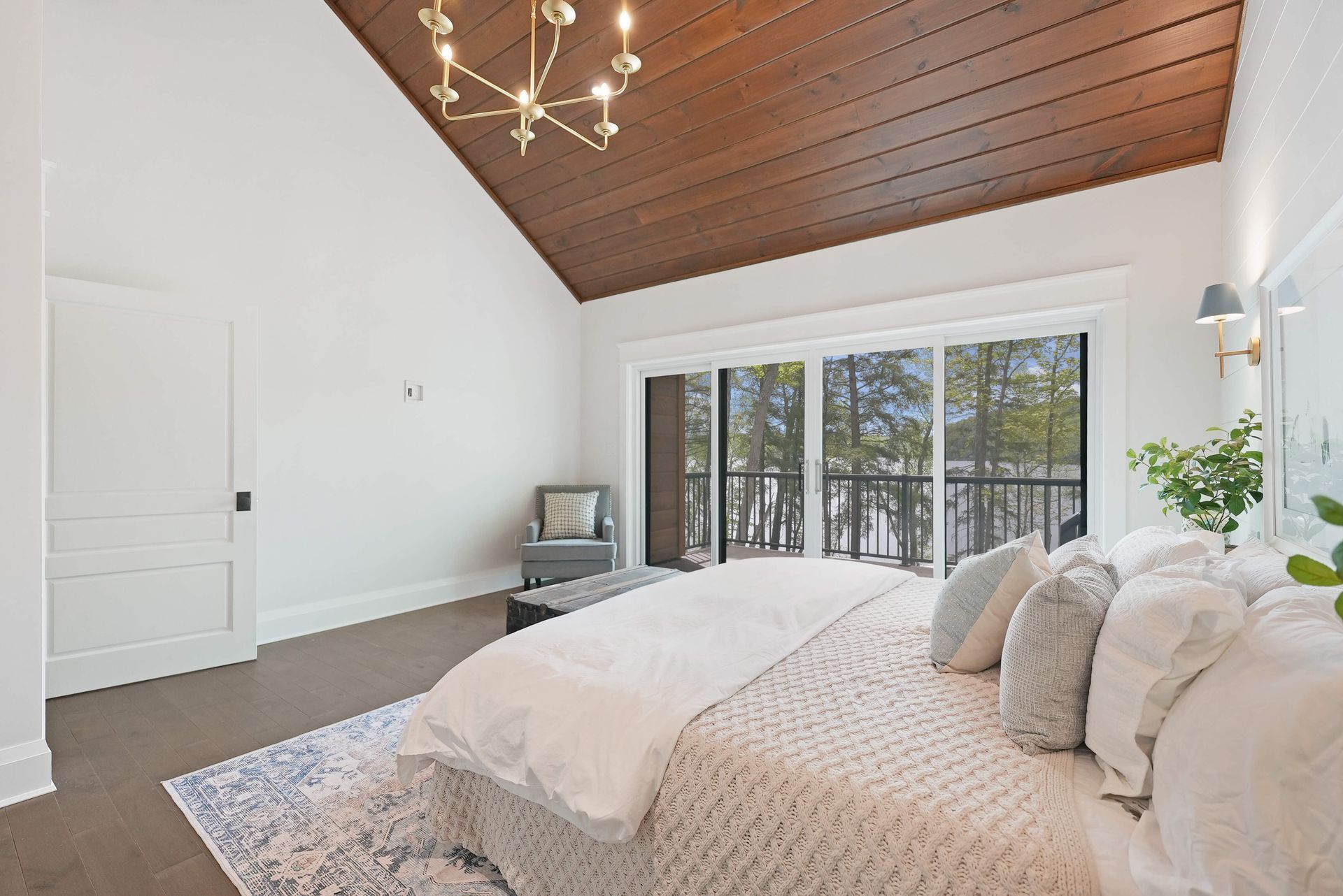 Bright bedroom with vaulted wood ceiling, white walls, and sliding doors to a balcony with trees beyond