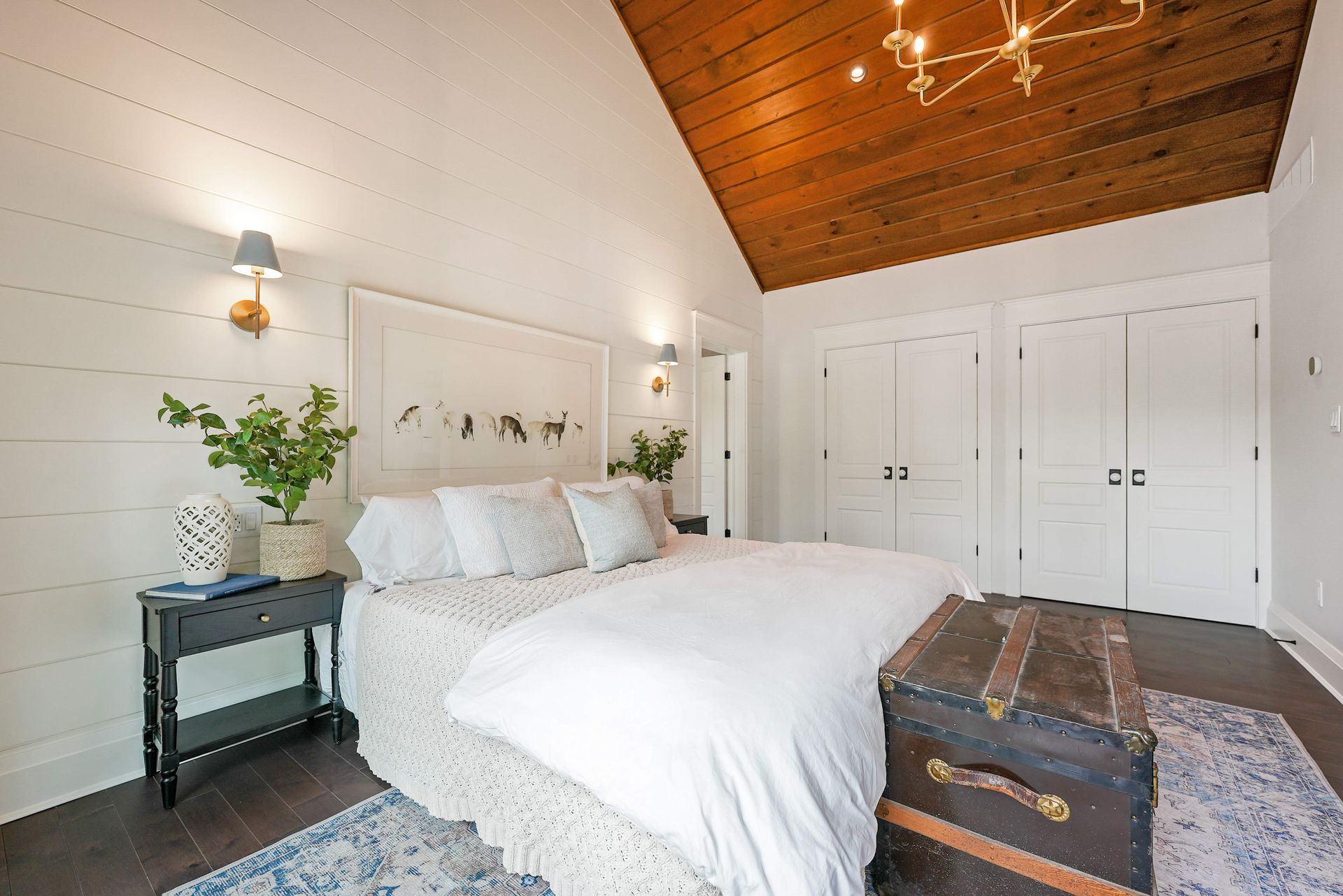Bright white bedroom with a wooden ceiling, large bed, and vintage trunk at the foot of the bed