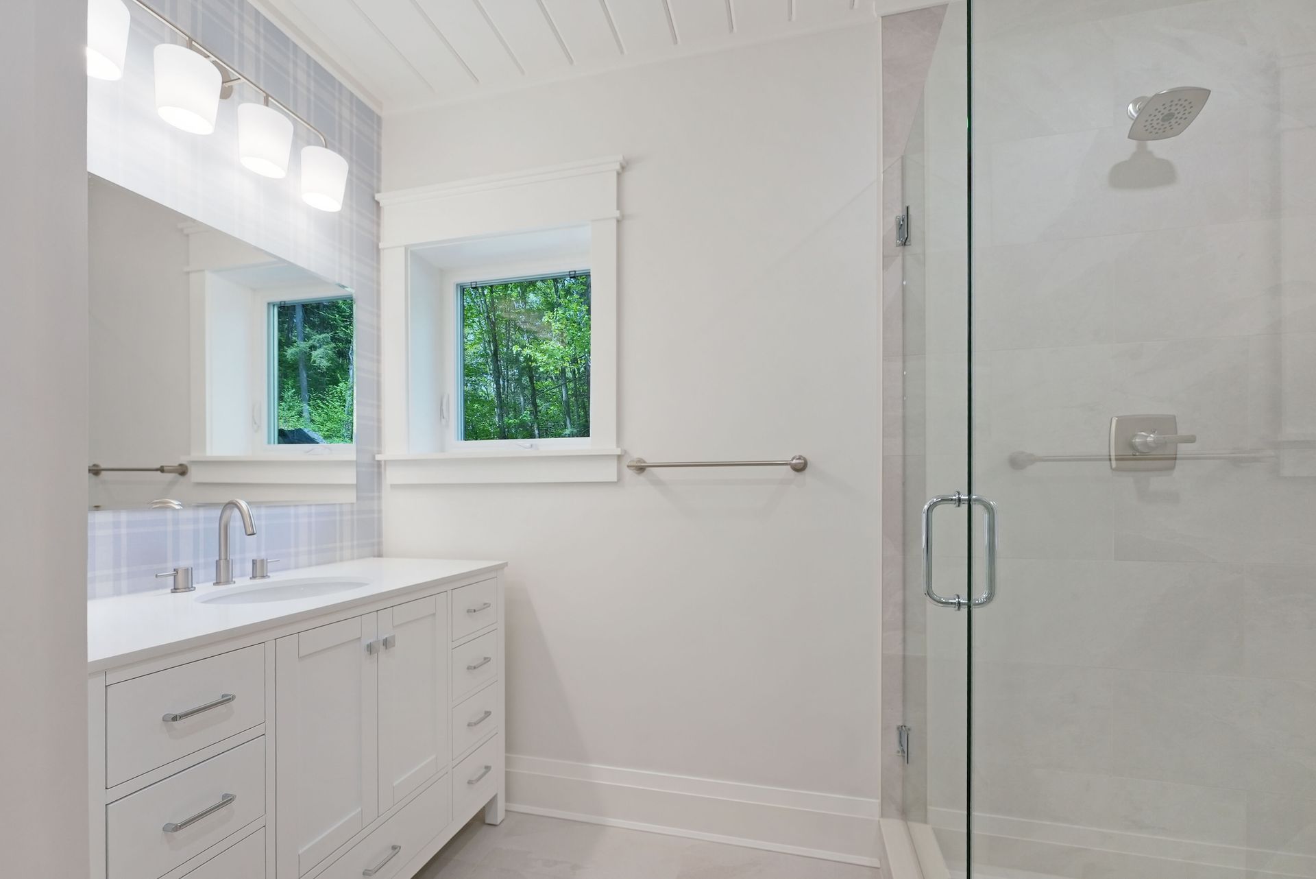 Bright white bathroom with double vanity, window, and glass shower enclosure