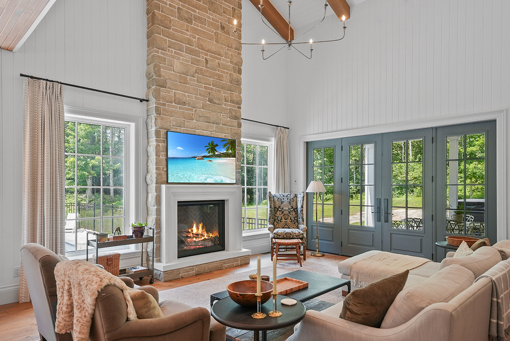 Rustic log cabin with large windows and stone retaining wall amid trees and greenery