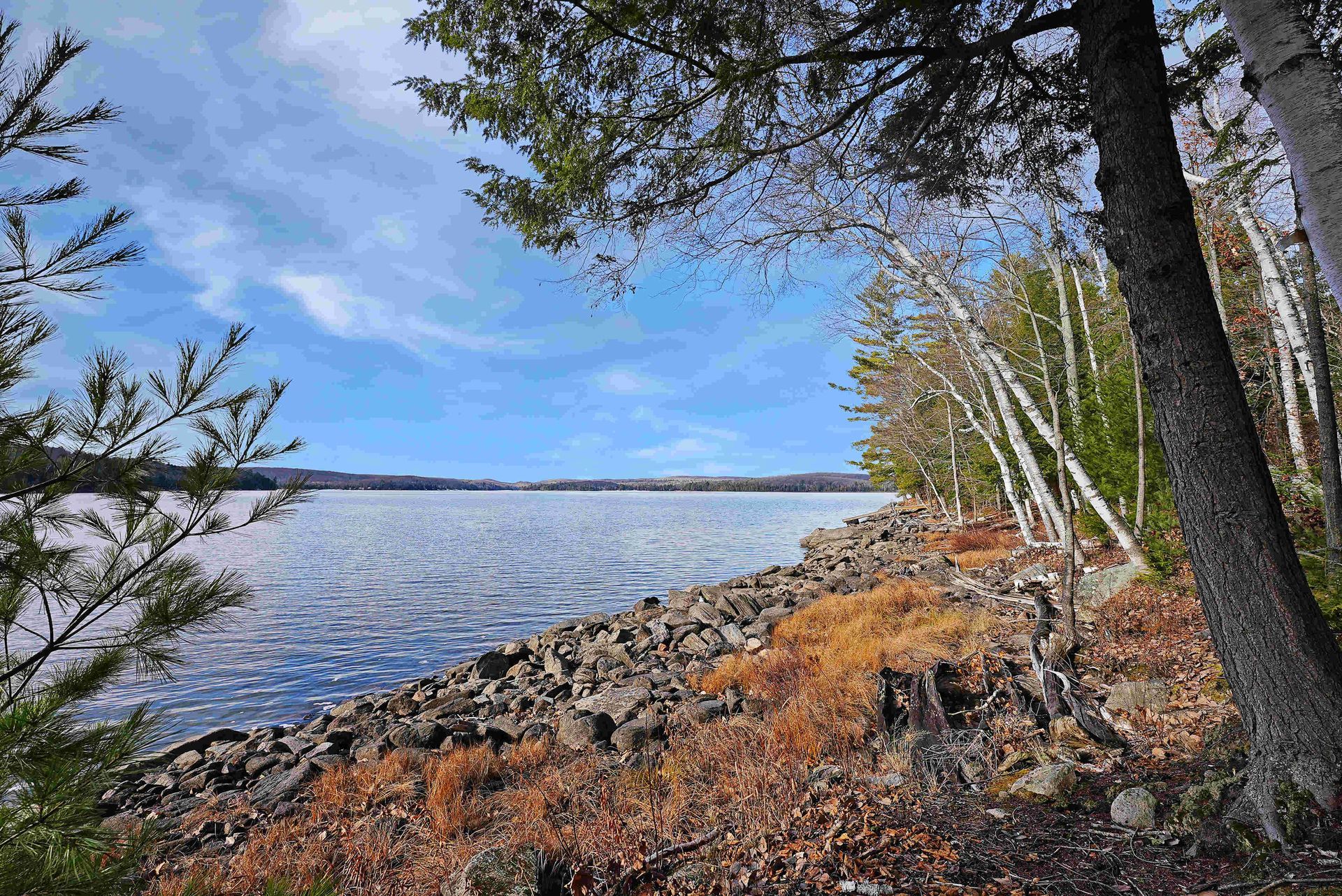 Rocky lakeshore with autumn trees and calm water under a blue sky