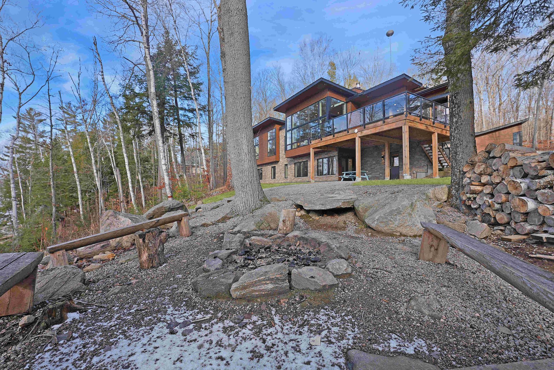 Rustic mountain cabin with wraparound porch among bare trees and rocky ground in early spring