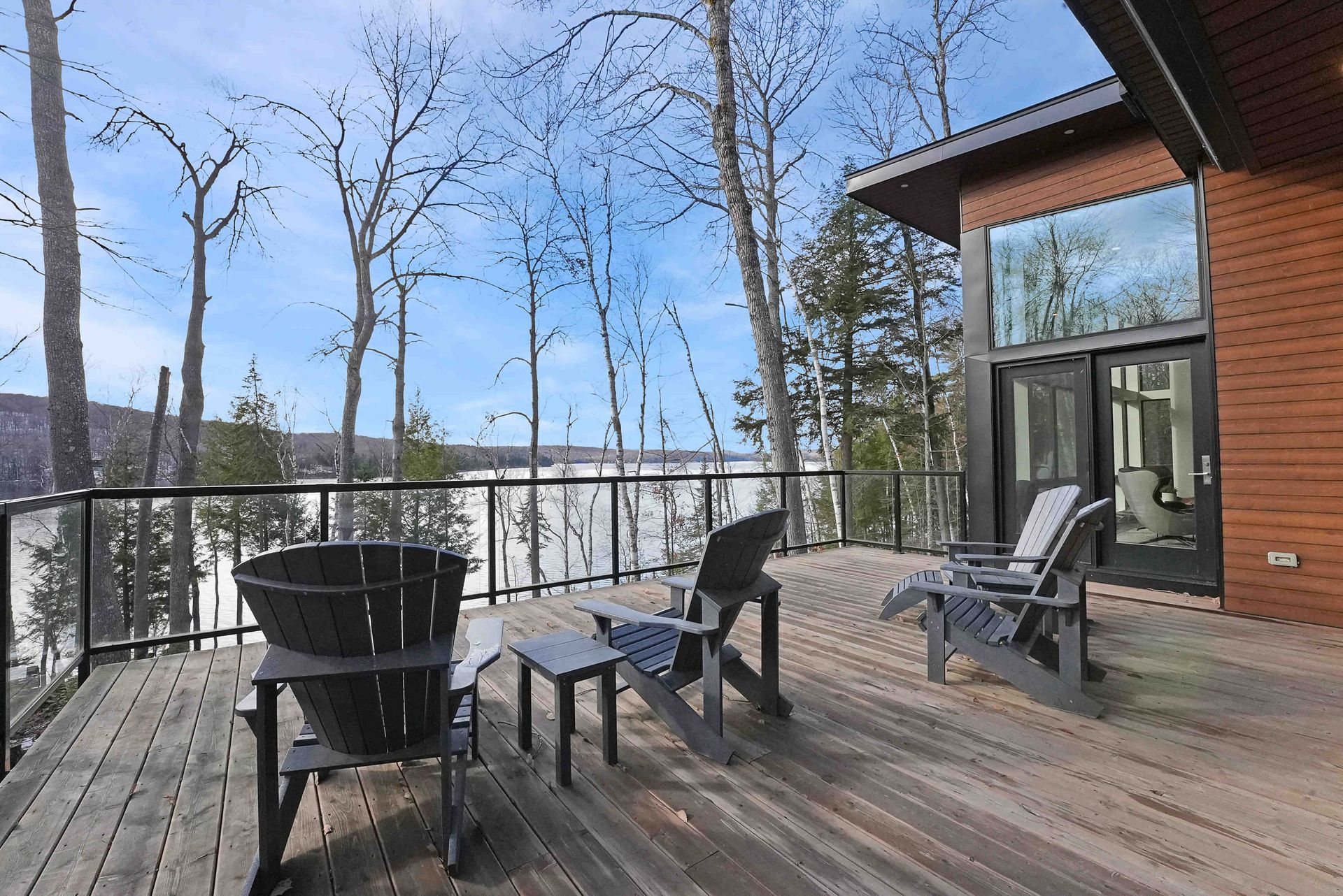 Wooden deck with black chairs and table overlooking bare trees and a blue winter sky