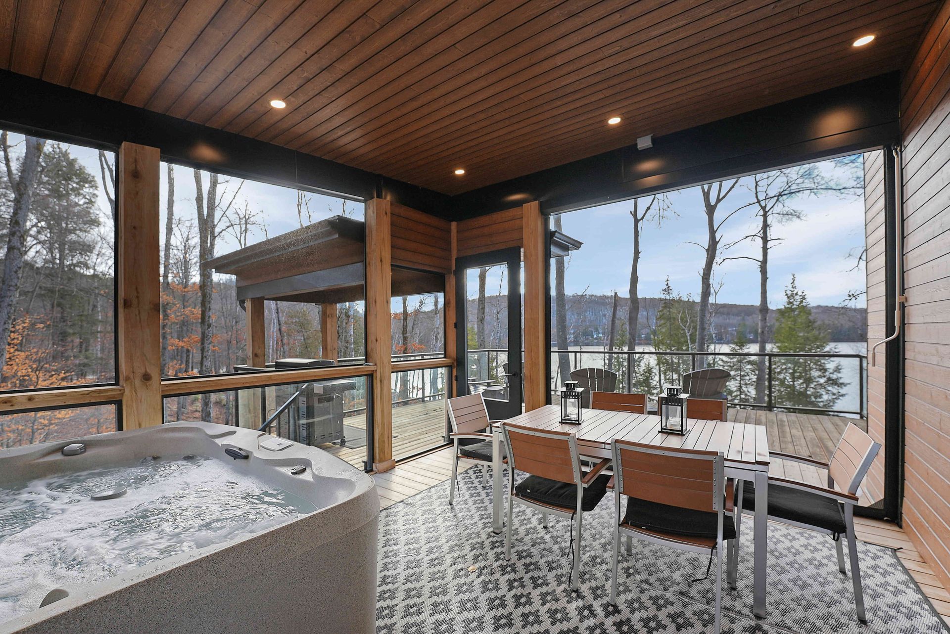 Modern patio dining area with a table, chairs, and a hot tub overlooking a snowy lake.