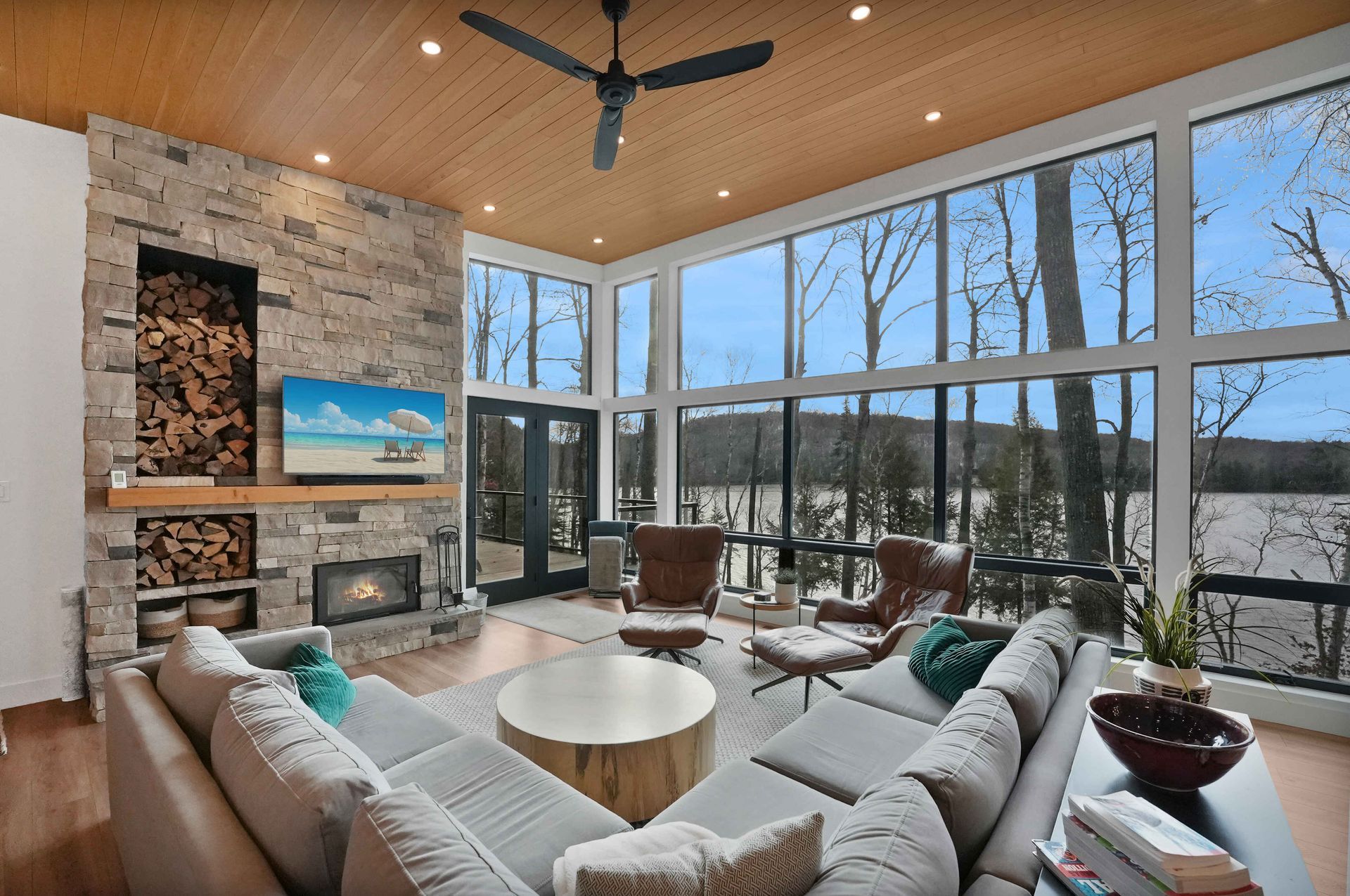 Modern living room with floor-to-ceiling windows, stone fireplace, white sofas, and lake view