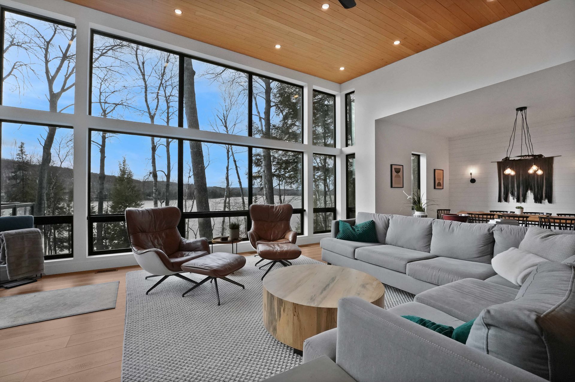Modern living room with large windows, gray sectional sofa, leather chairs, and snowy outdoor view
