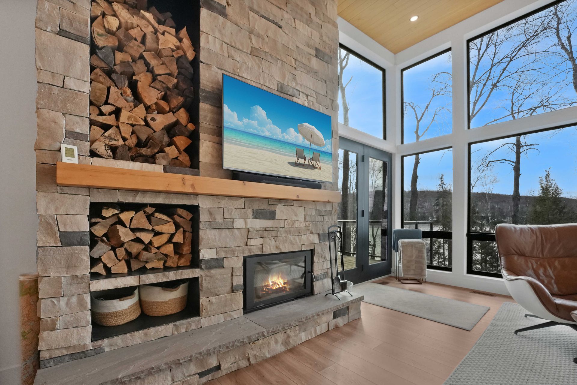 Modern living room with stone fireplace, stacked firewood, and large windows with mountain view