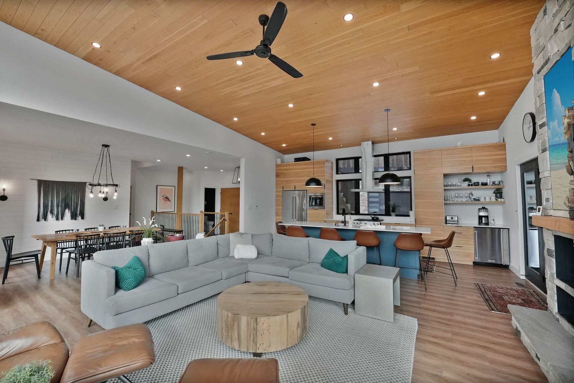 Modern open-plan living room with sectional sofa, wood ceiling, dining area, and kitchen island