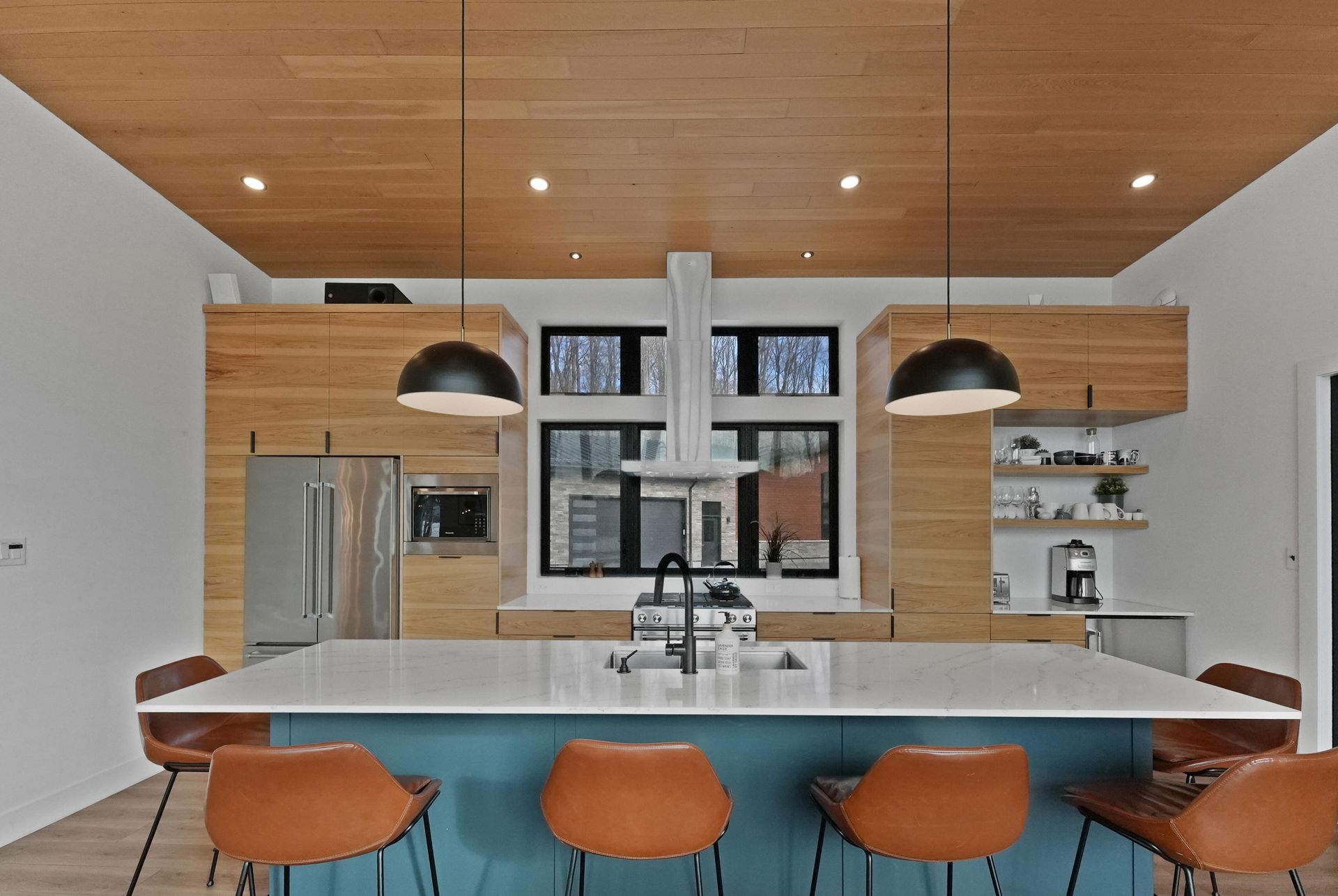 Modern kitchen with white island, wood cabinets, pendant lights, and orange bar stools