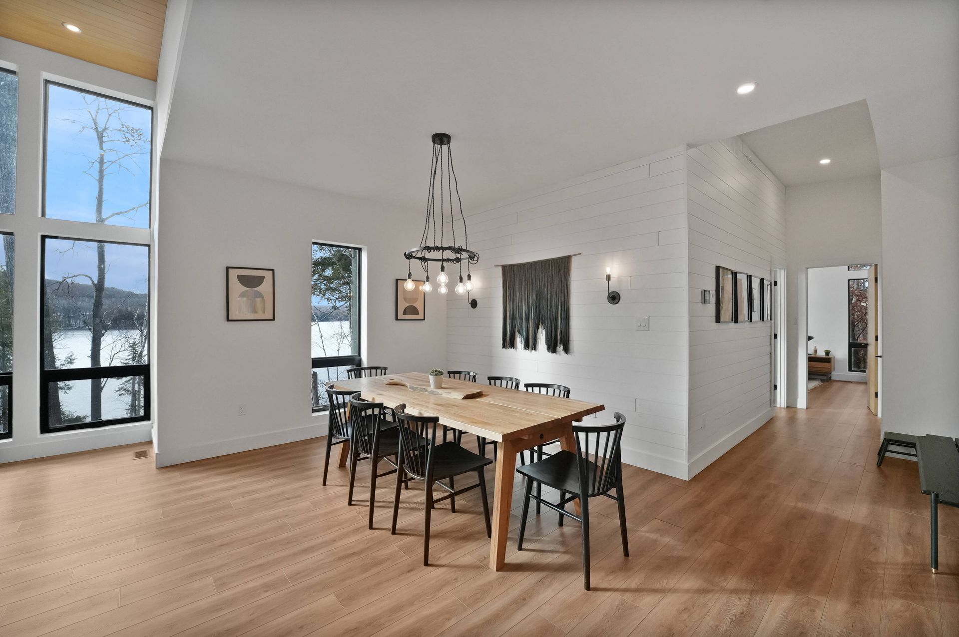 Bright dining room with long wooden table, black chairs, chandelier, and large windows overlooking outdoors