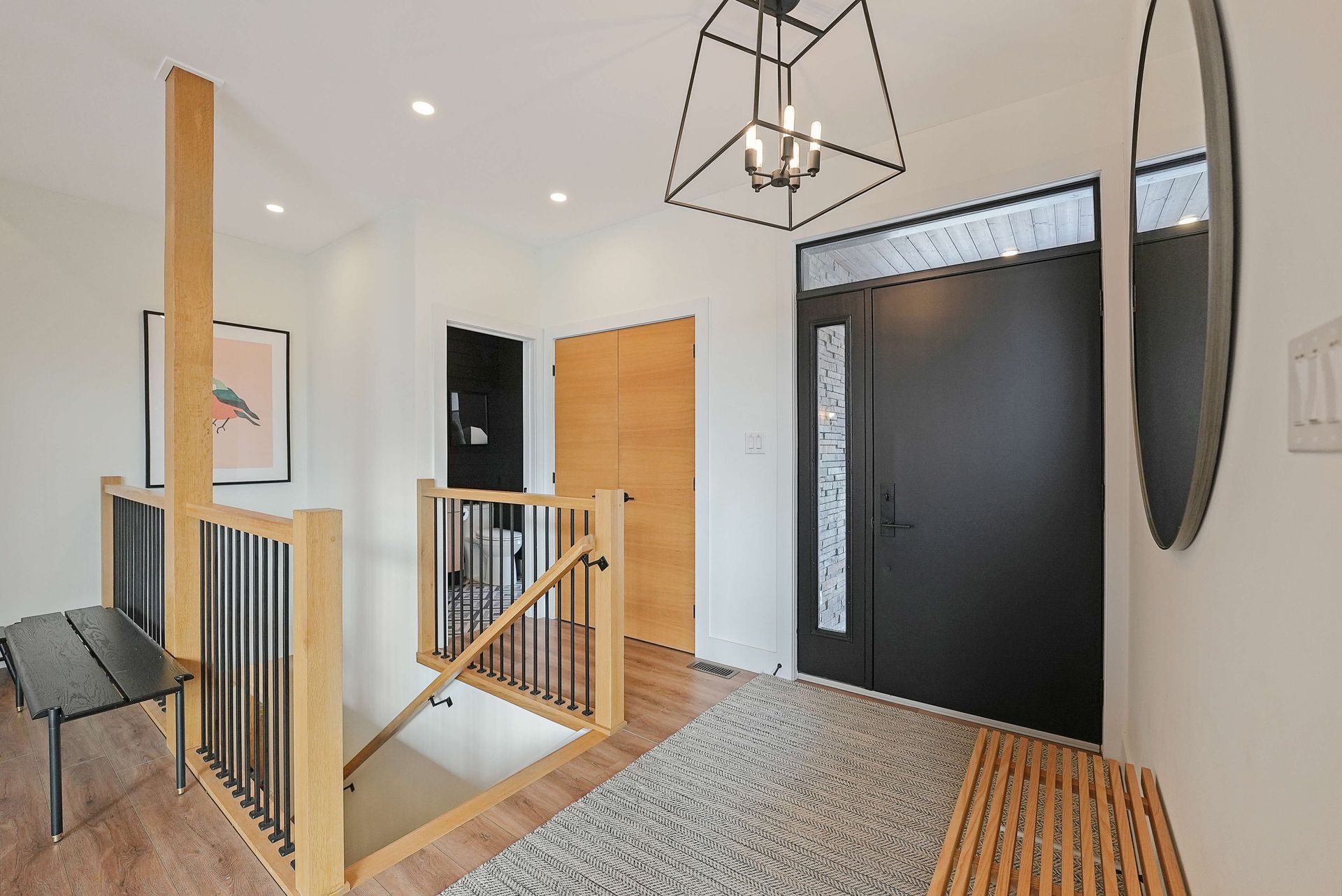 Modern home entryway with black front door, wood accents, staircase railing, and bench seating