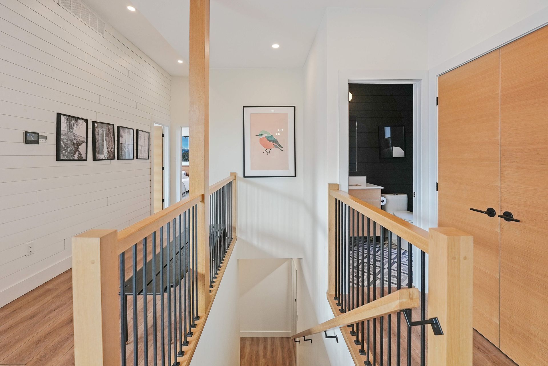 Bright hallway landing with wood railings, framed art, and a doorway at the end