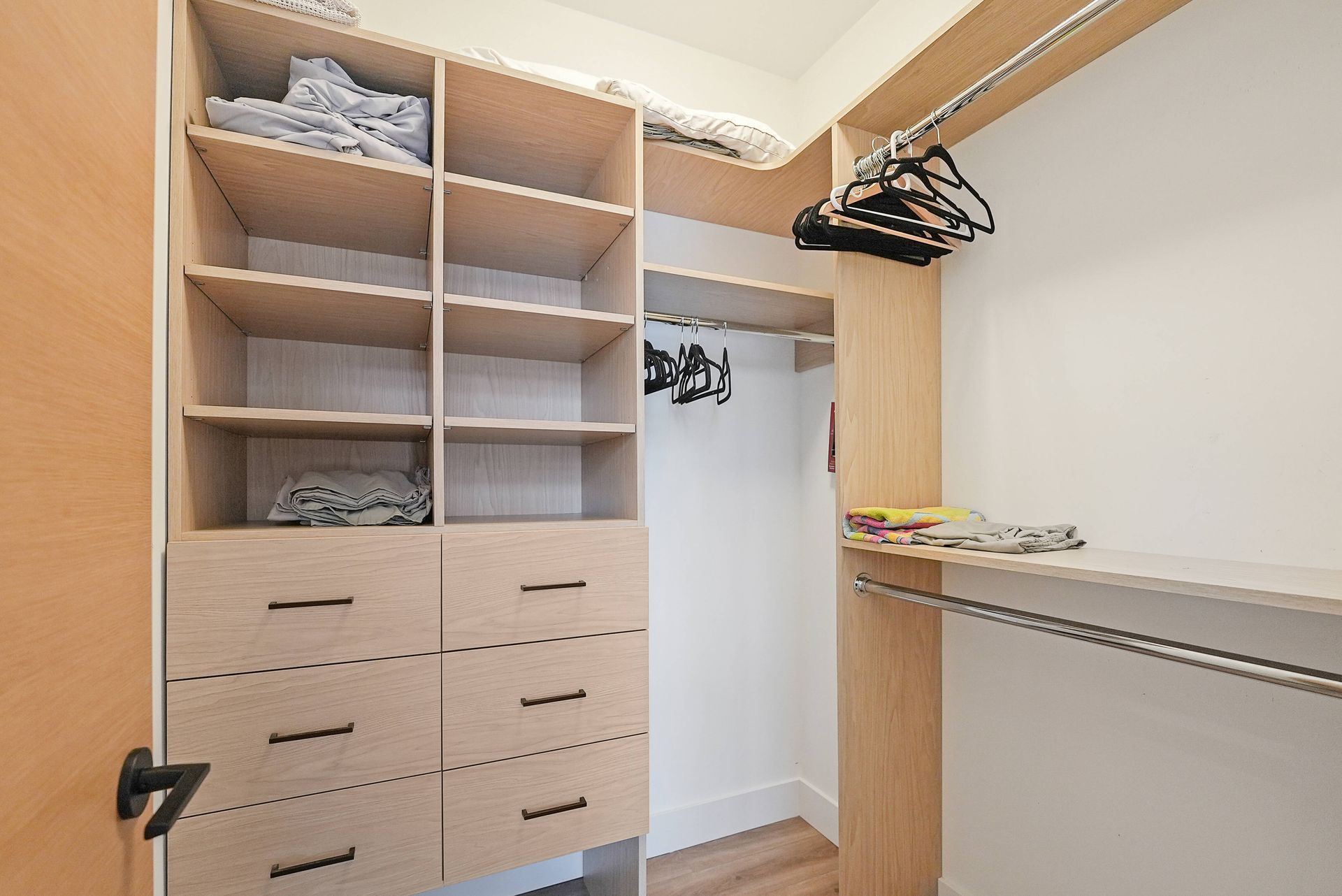 Built-in closet with open shelves, drawers, hanging rods, and clothes hangers in a bright room.